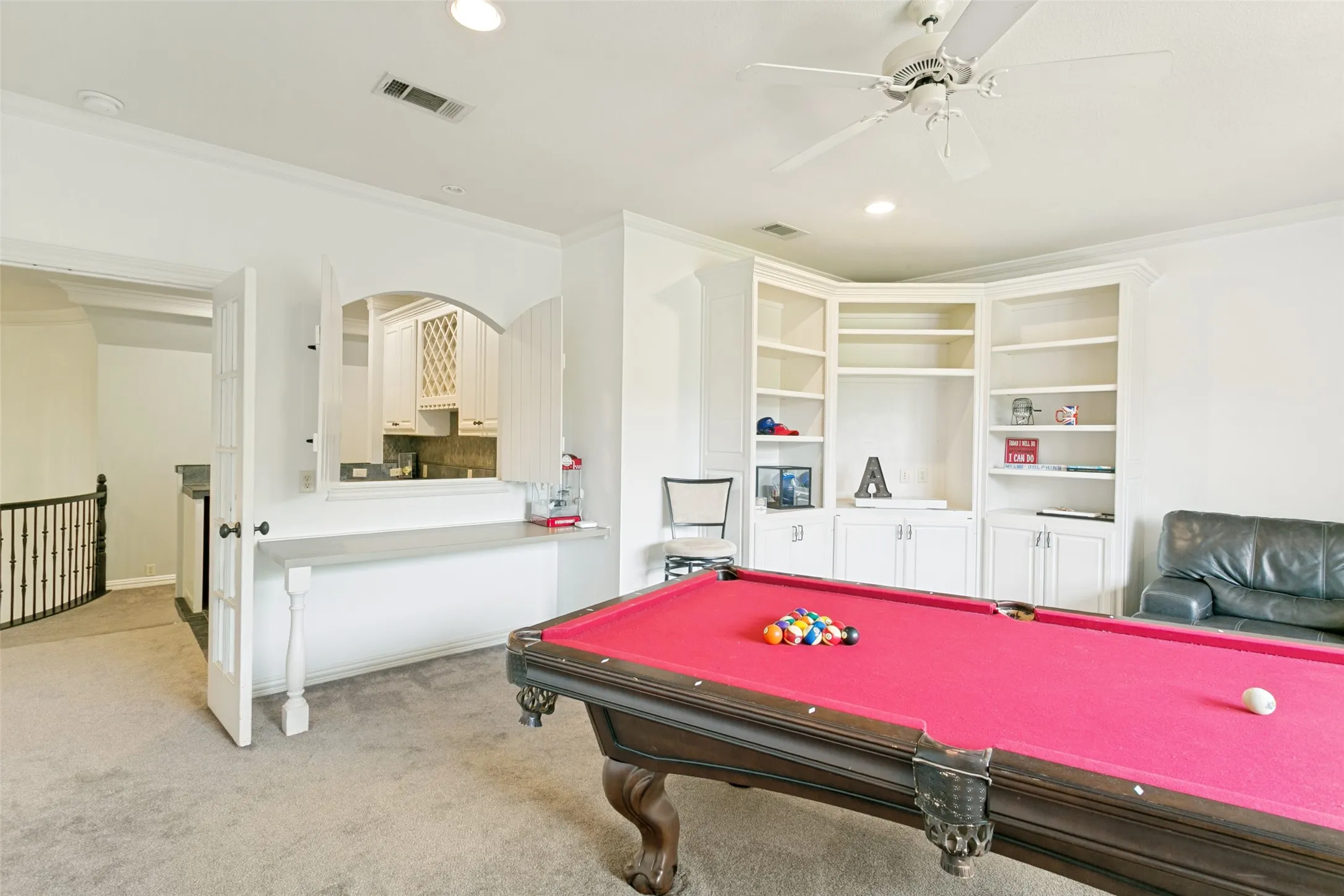 Carpeted room featuring a built-in entertainment center with open shelving and lower cabinetry, a ceiling fan with integrated lighting, recessed lighting, and a built-in pass-through window with a counter