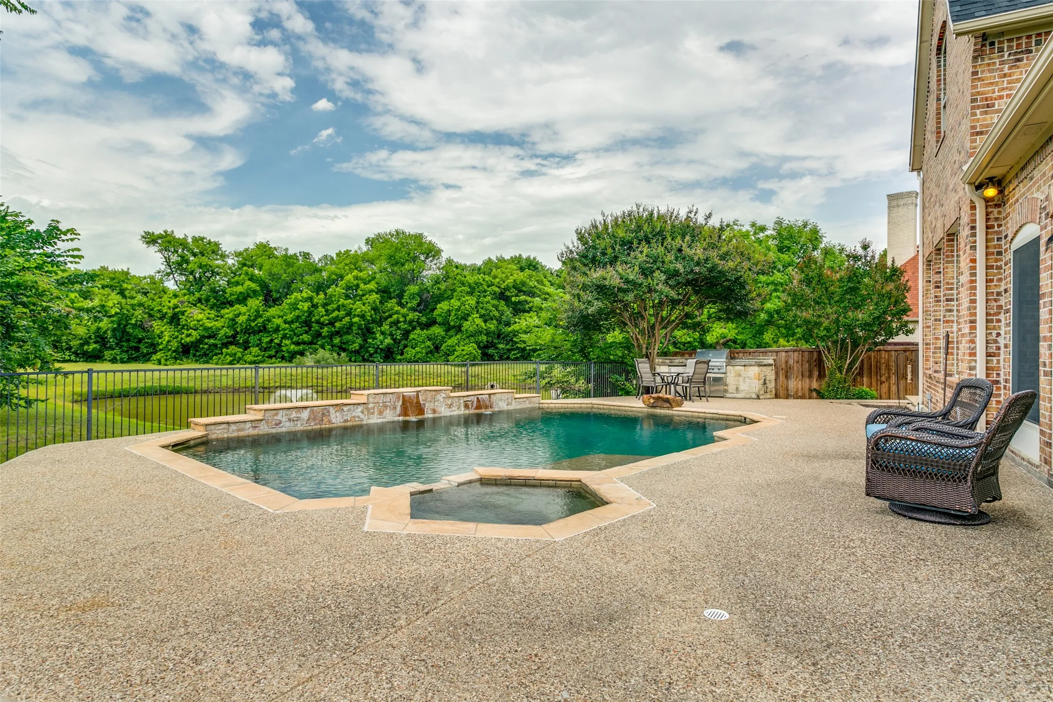 Expansive backyard featuring a large swimming pool with an integrated spa, stone waterfall features, and a surrounding aggregate concrete patio
