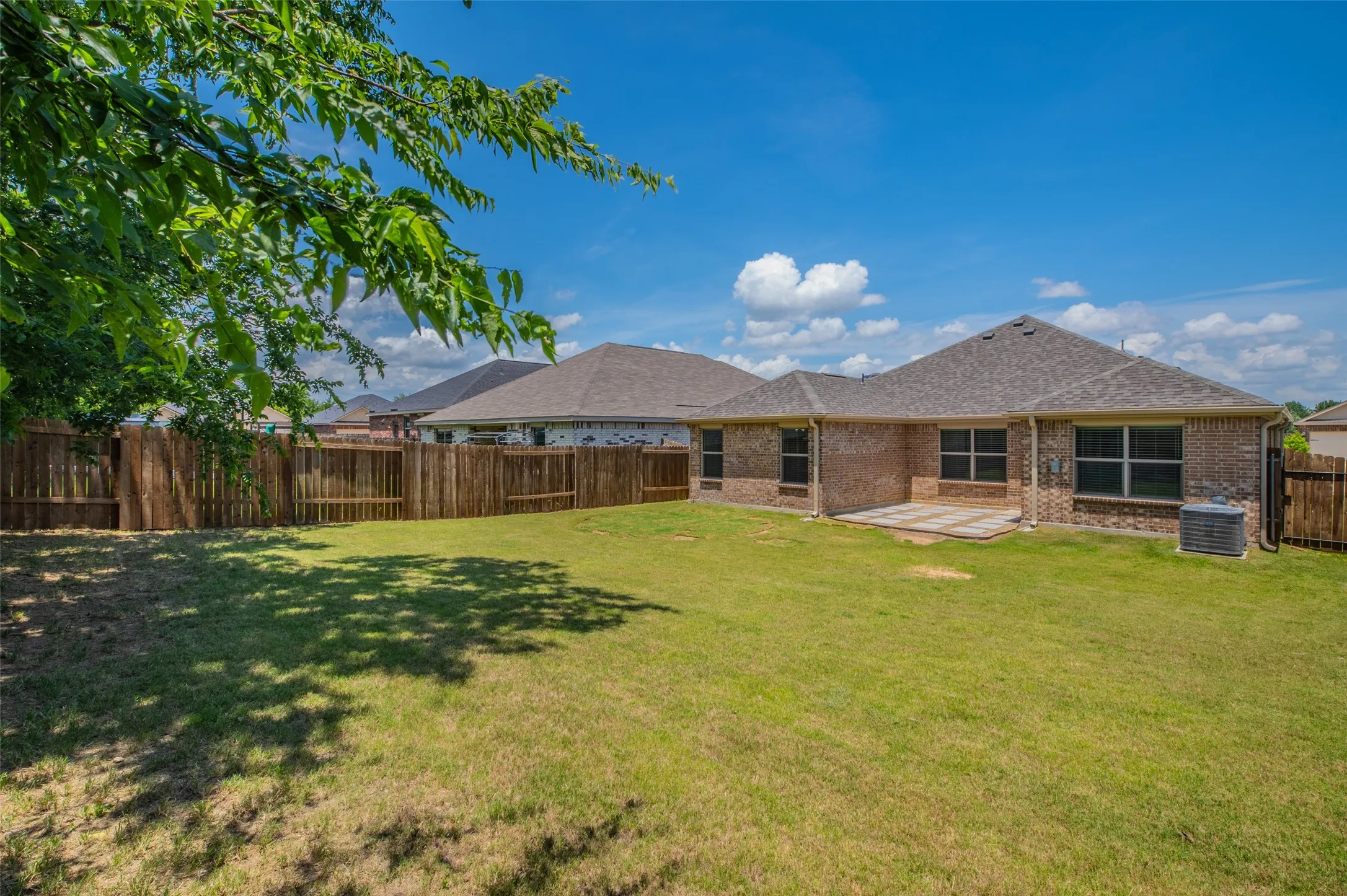 Expansive backyard featuring a manicured lawn, a full wood privacy fence, and a brick exterior with multiple windows
