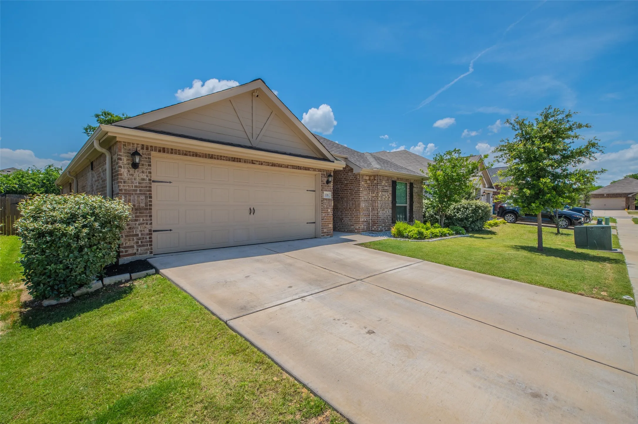 Brick exterior with a two-car garage featuring decorative hardware, concrete driveway, and established landscaping