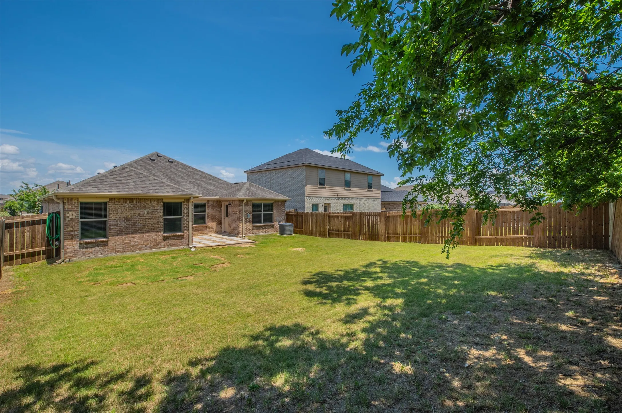 Expansive backyard featuring a manicured lawn, a full wood privacy fence, and a stone patio