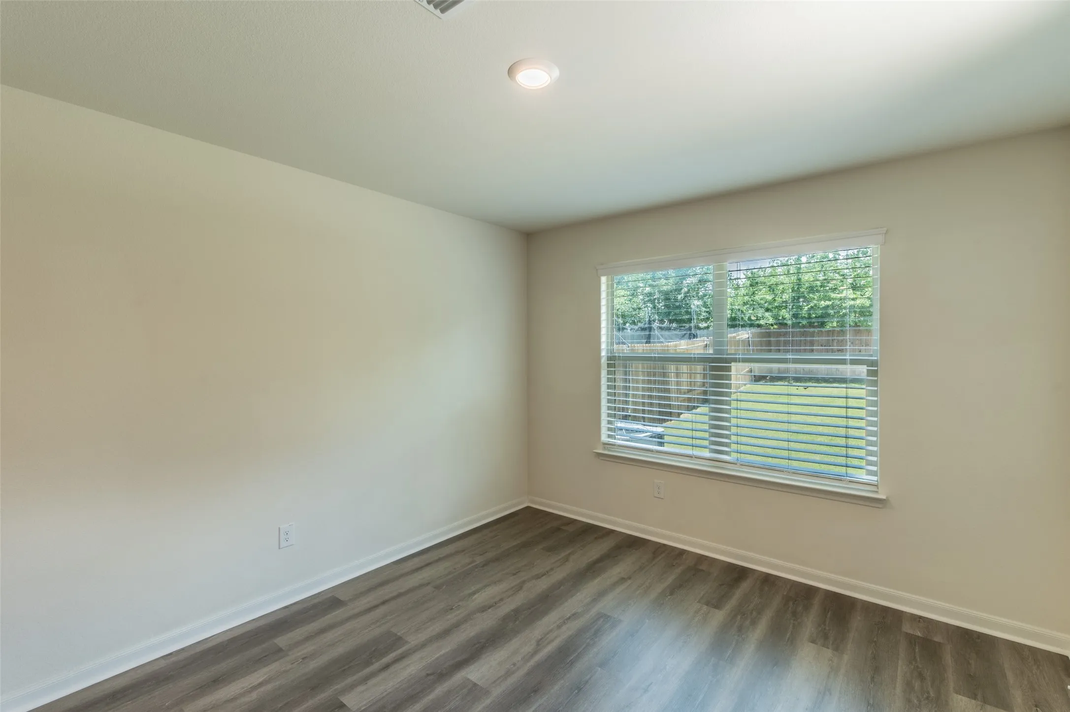 Primary bedroom with wood-finish flooring, neutral wall paint, and a large window with blinds