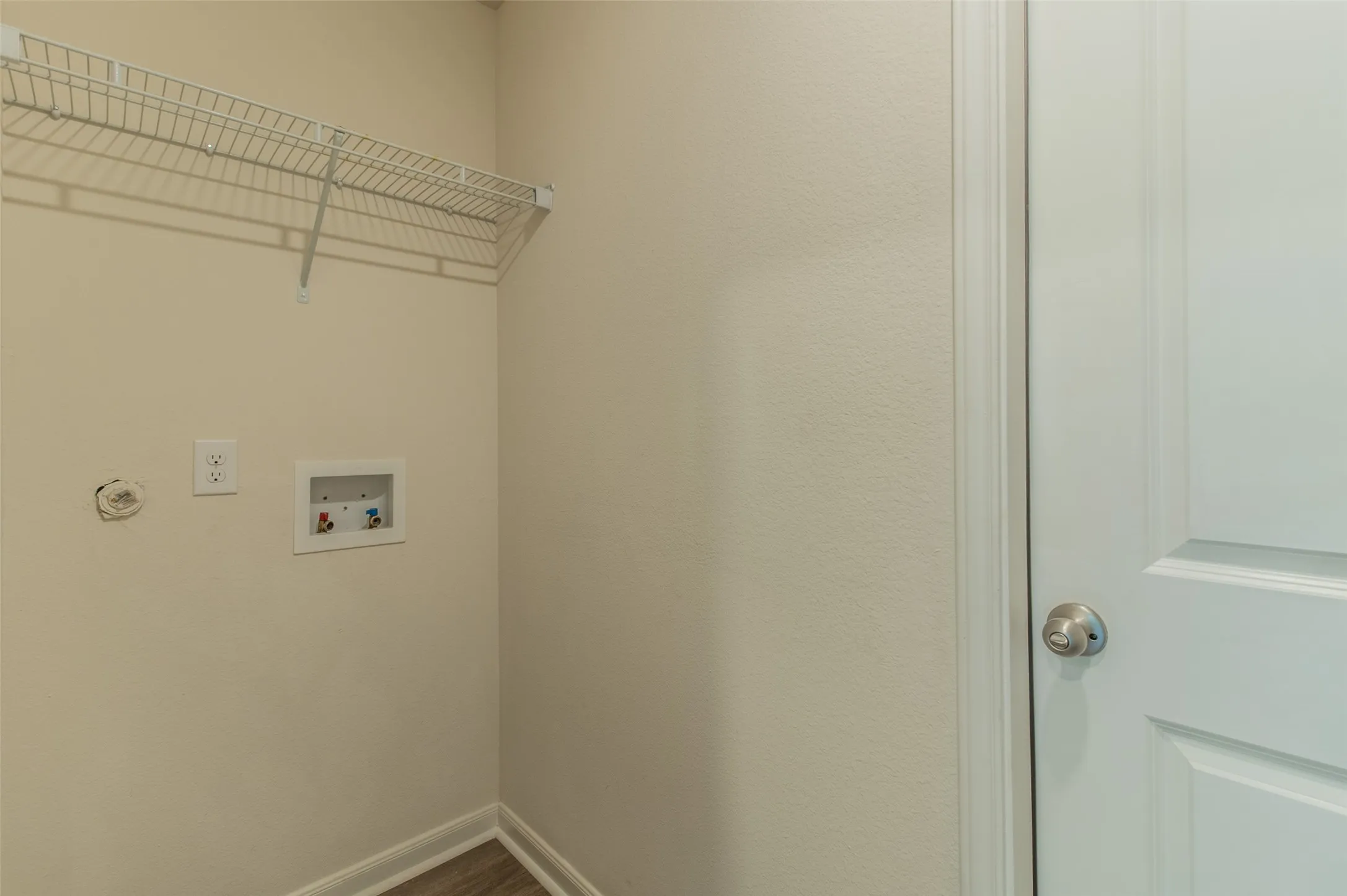 Dedicated utility area featuring a wire shelf, wall-mounted electrical outlet, and plumbing hookups