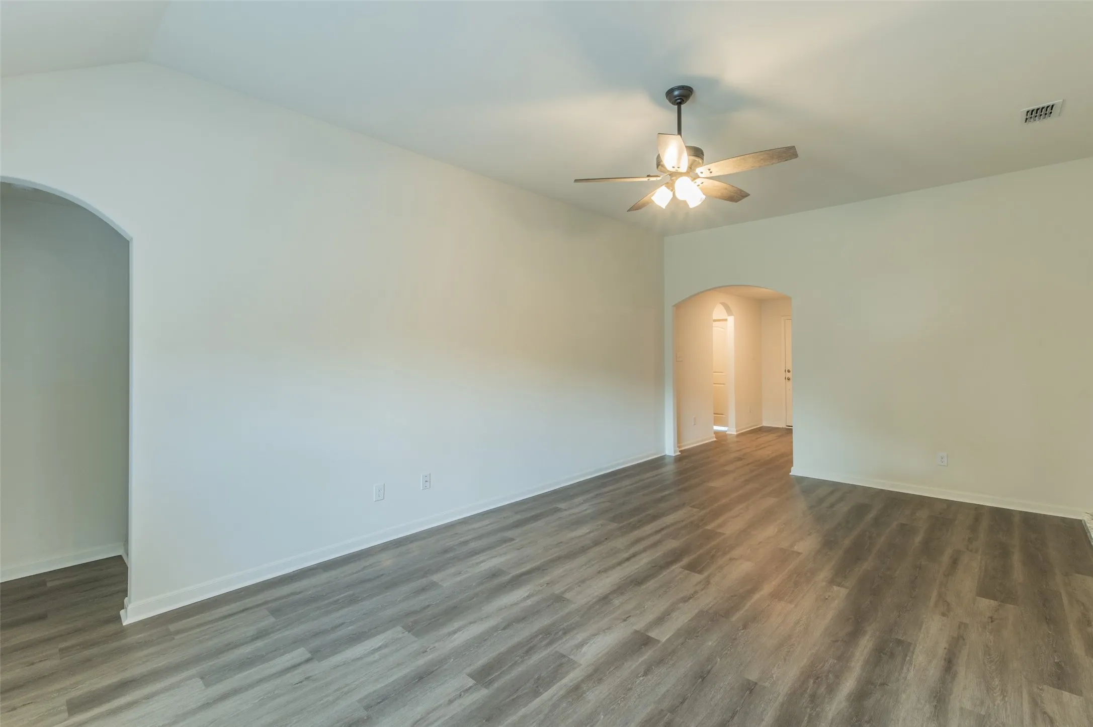Spacious interior featuring luxury vinyl wood-finish flooring, neutral paint palette, arched doorways, and a ceiling fan with integrated lighting