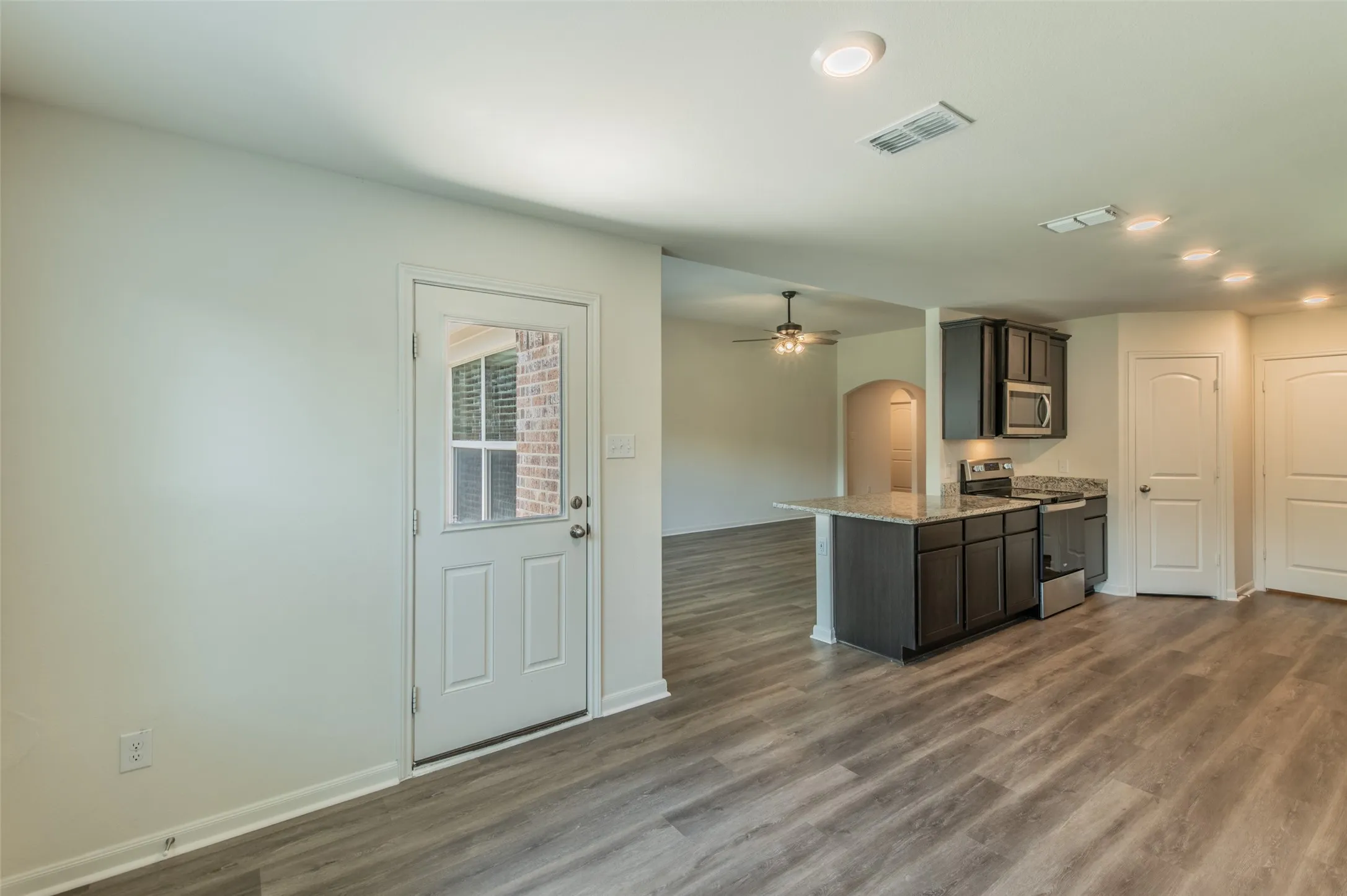 Modern kitchen featuring dark cabinetry, stainless steel appliances, a granite countertop, and luxury vinyl wood-finish flooring