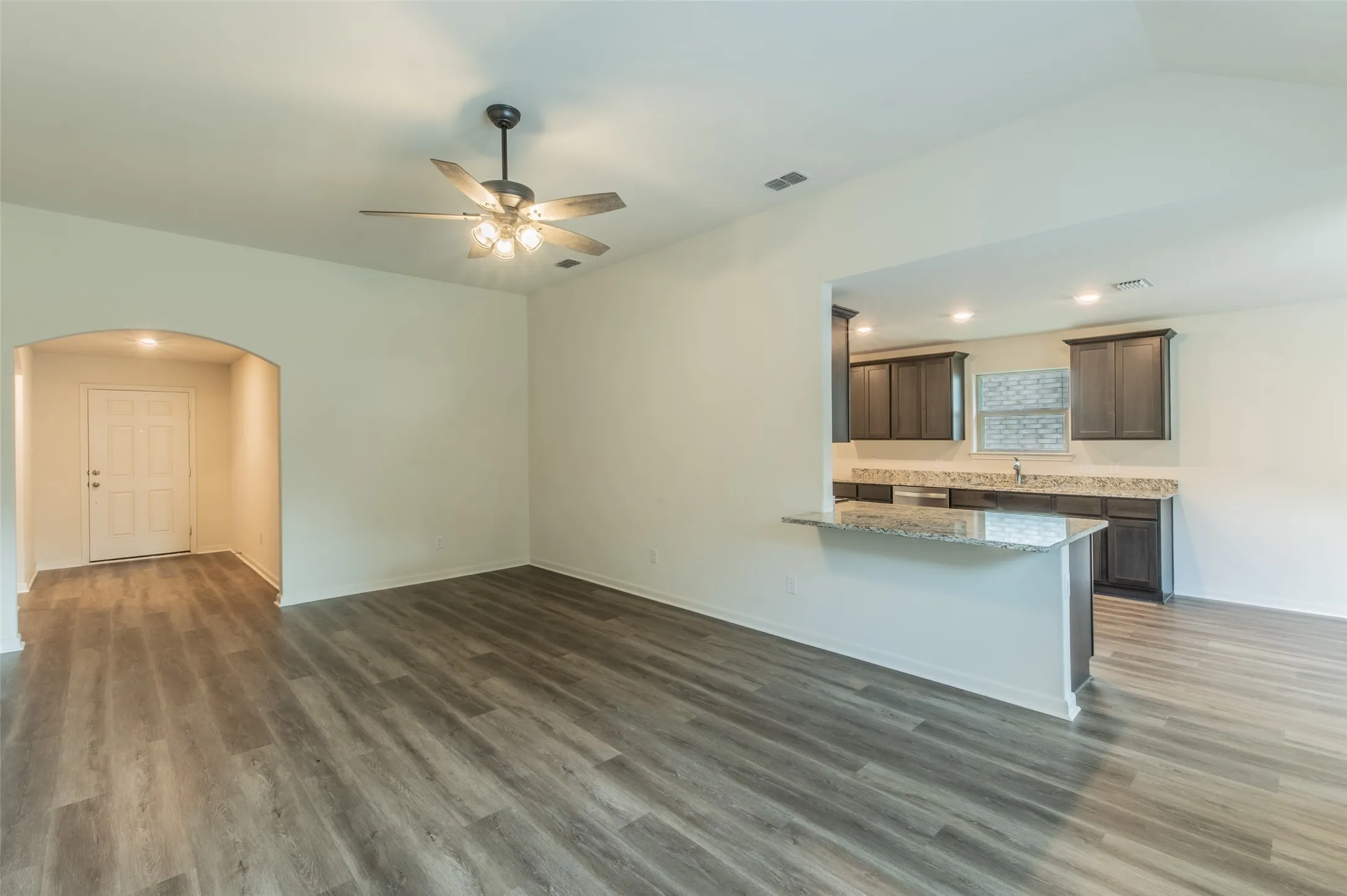 Open concept living space featuring luxury vinyl wood-finish flooring, a ceiling fan, and an arched entry