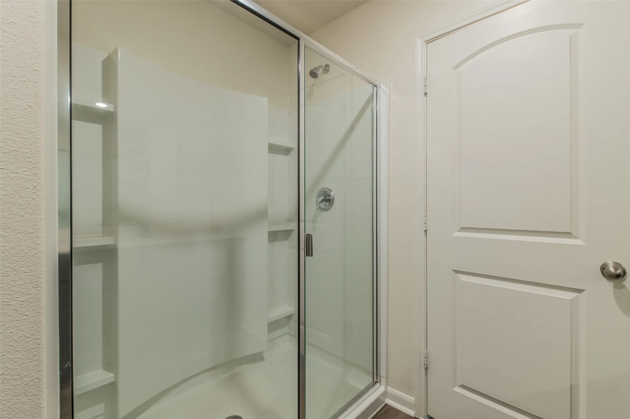 Glass-enclosed shower with integrated shelving and a chrome showerhead