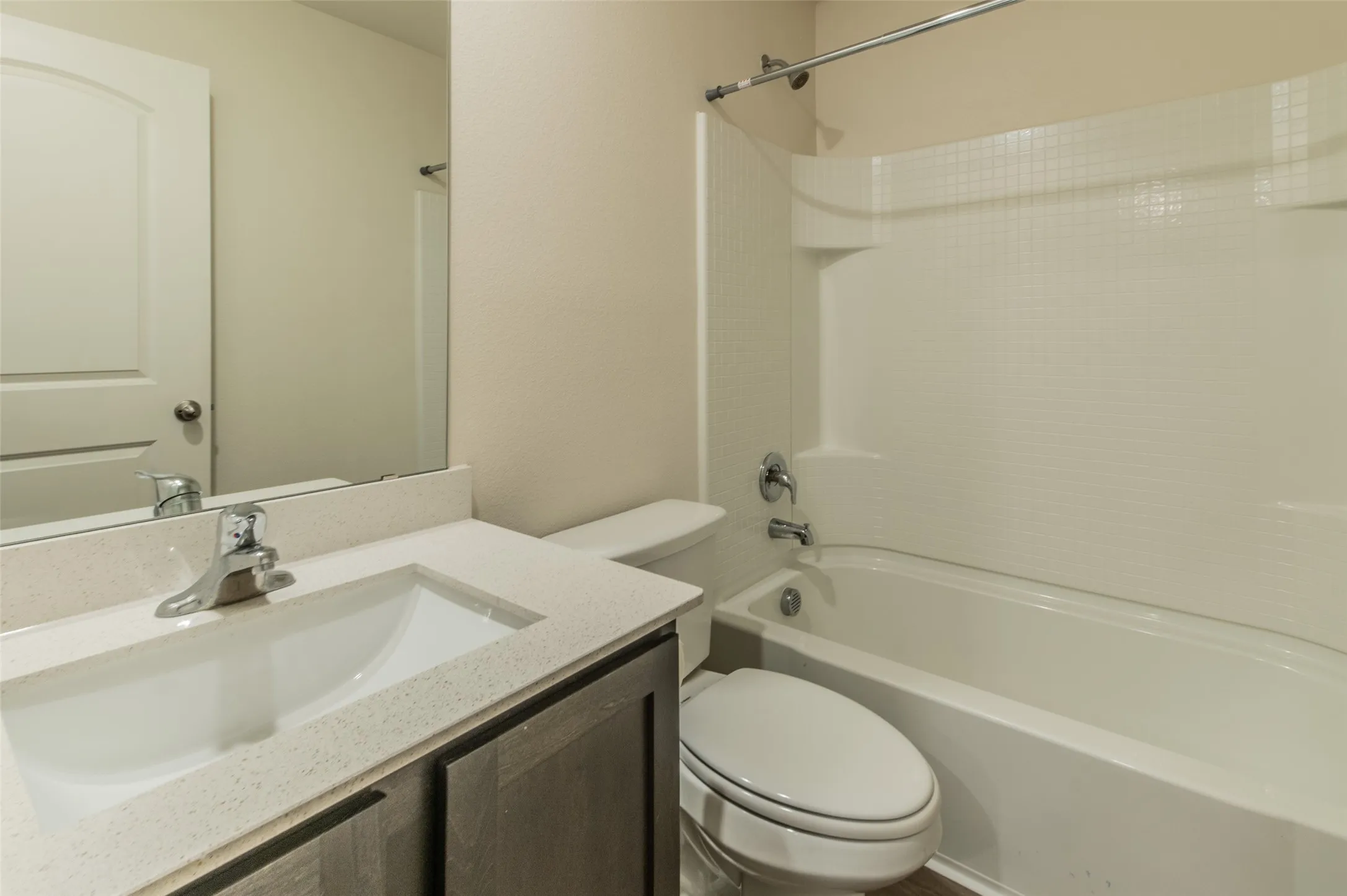 Bathroom featuring a tub/shower combination with a textured surround, a white toilet, and a vanity with a light-colored countertop and undermount sink