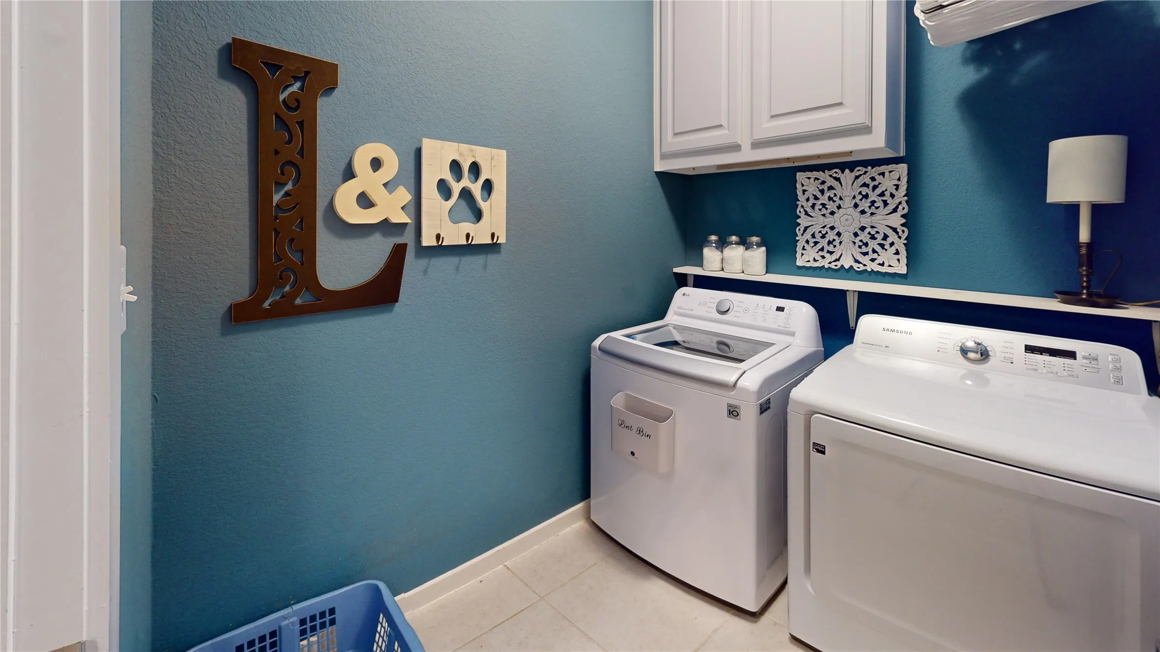 Dedicated laundry area featuring white wall cabinetry, a built-in shelving unit, and tile flooring