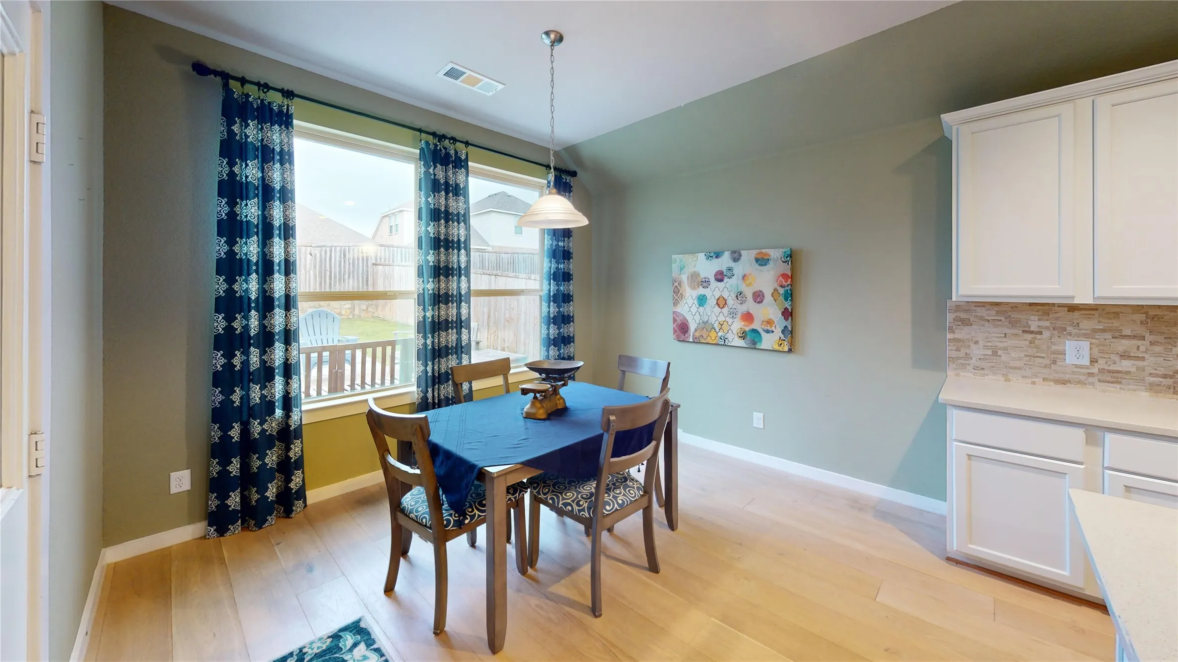 Dining area with wood-finish flooring, ample natural light from a large window, a ceiling-mounted light fixture, and an open concept layout connecting to the kitchen