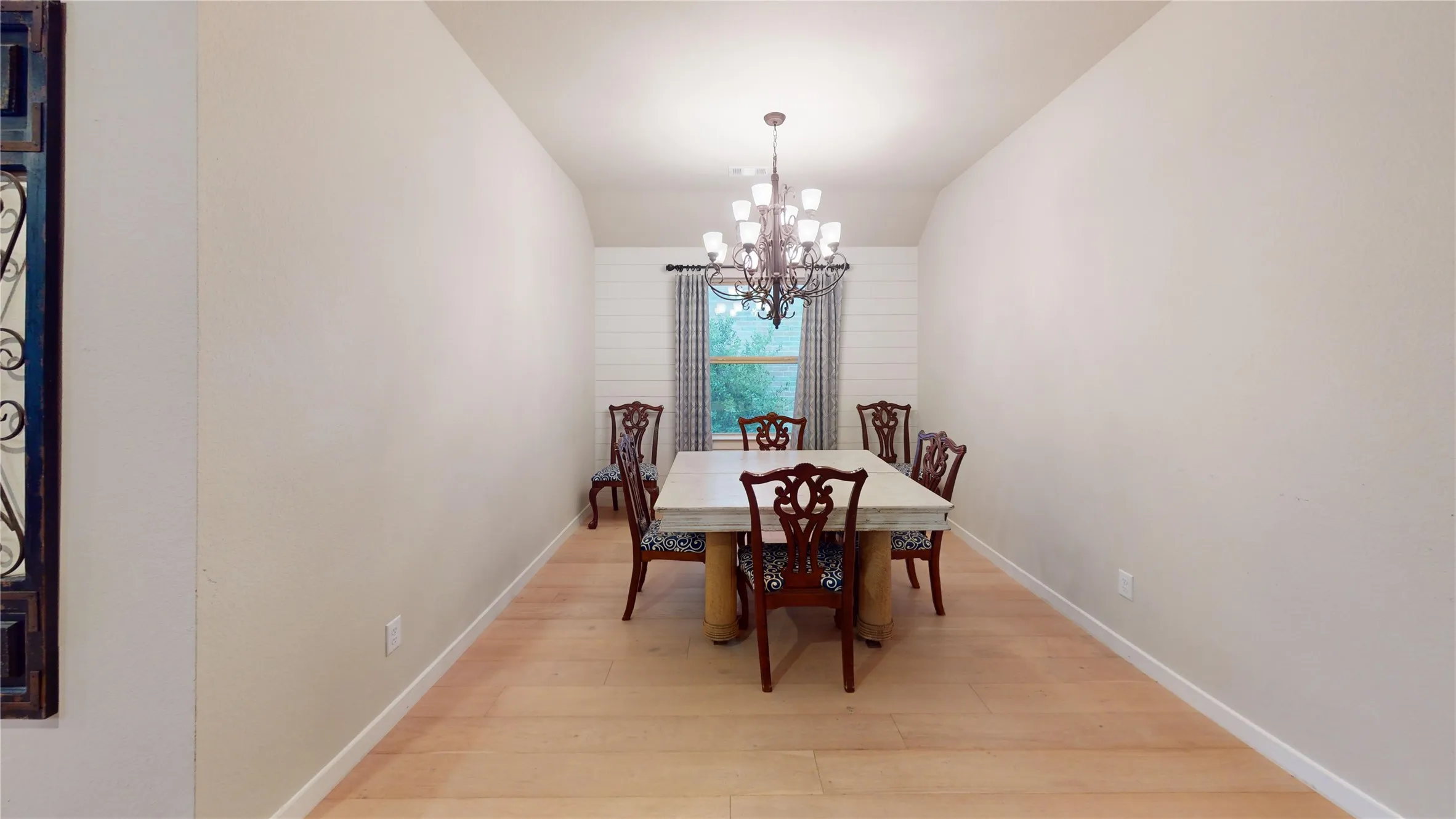 Dedicated dining space featuring a prominent chandelier, light wood-finish flooring, and a window with shiplap detailing
