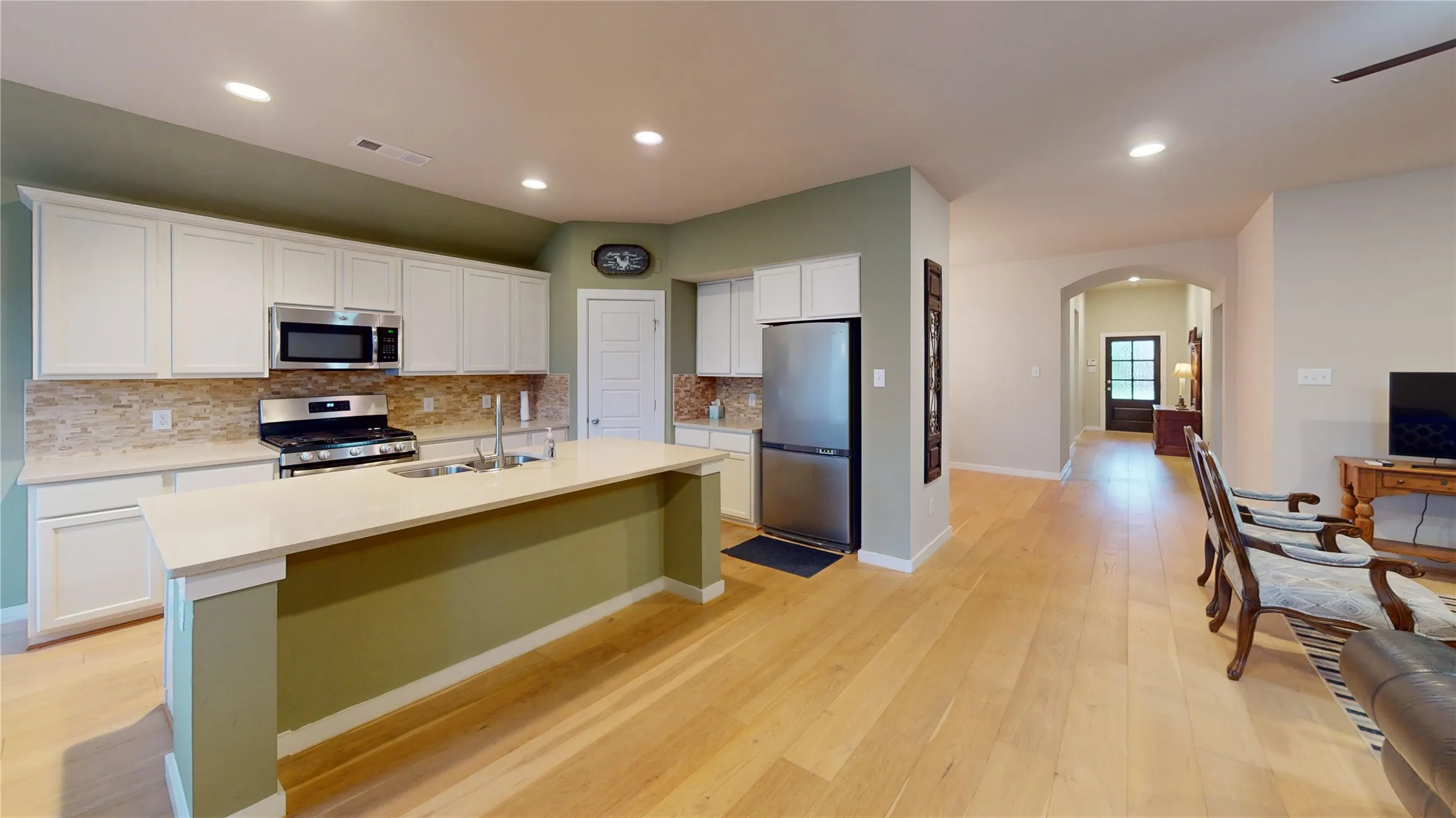 Spacious kitchen featuring an island with an undermount sink, light-toned countertops, white cabinetry, a neutral-toned backsplash, and stainless steel appliances