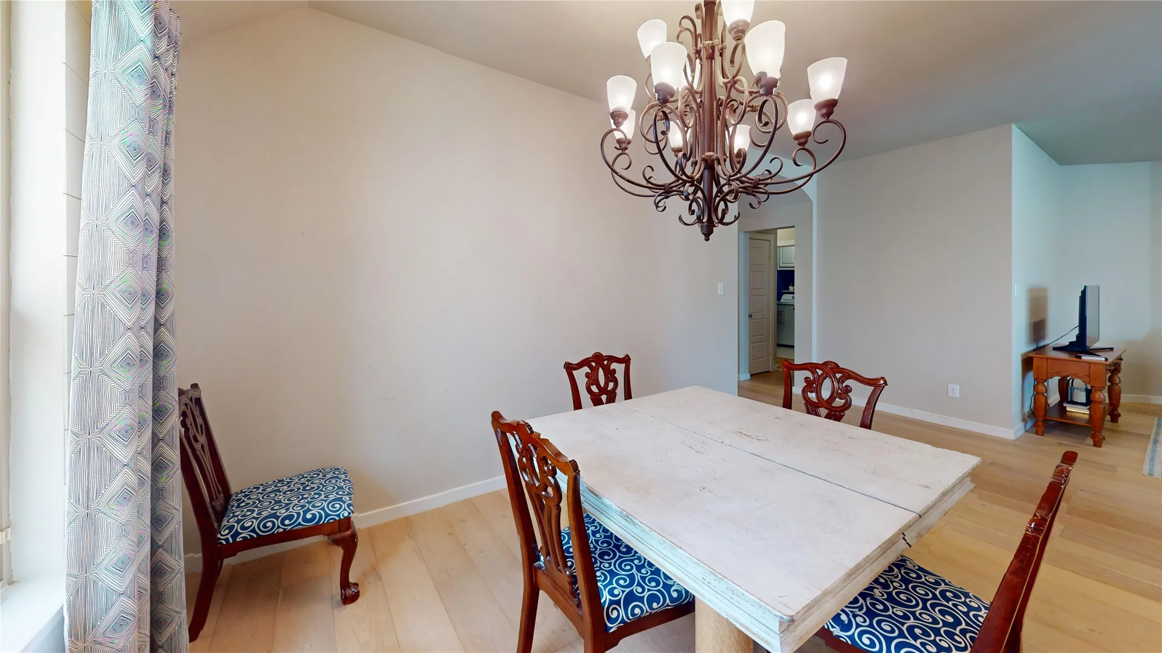 Spacious room with a decorative multi-bulb chandelier, light wood-finish flooring, and neutral wall paint