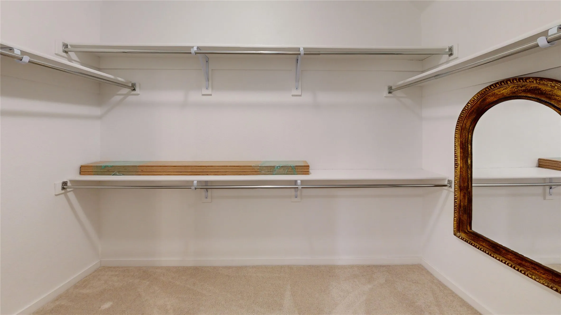 Carpeted closet space featuring white walls and a multi-level shelving system with chrome hanging rods