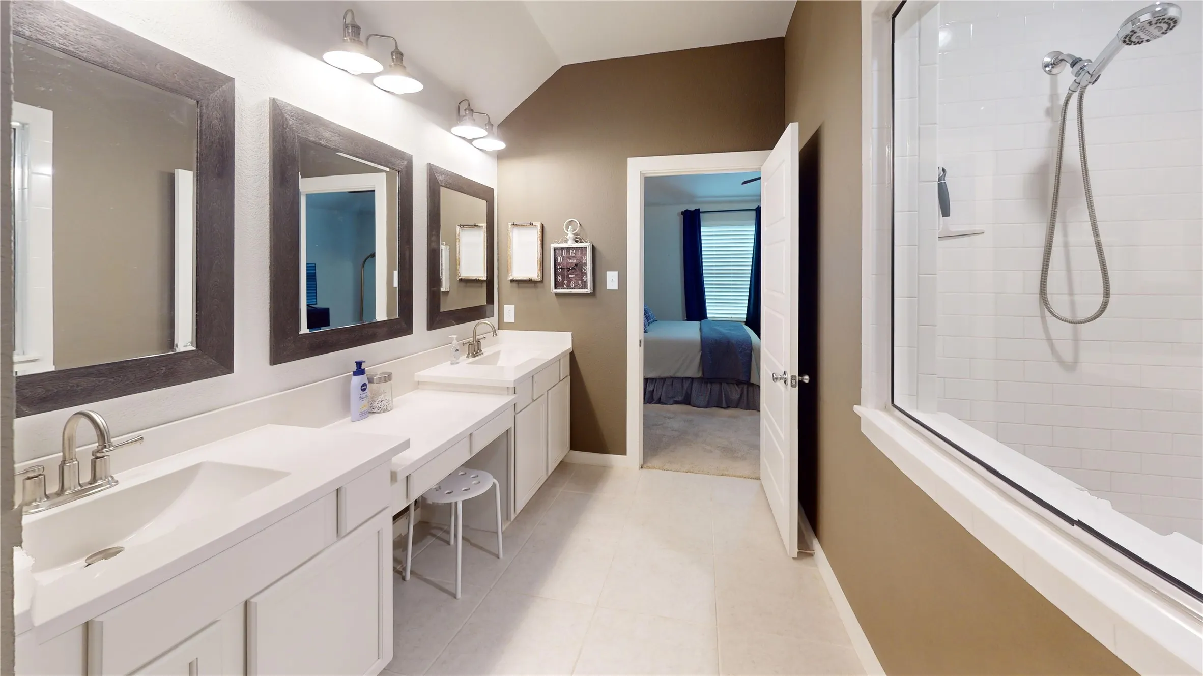 Bathroom featuring dual vanity sinks, white cabinetry, a built-in makeup area, and a glass-enclosed shower with white subway tile