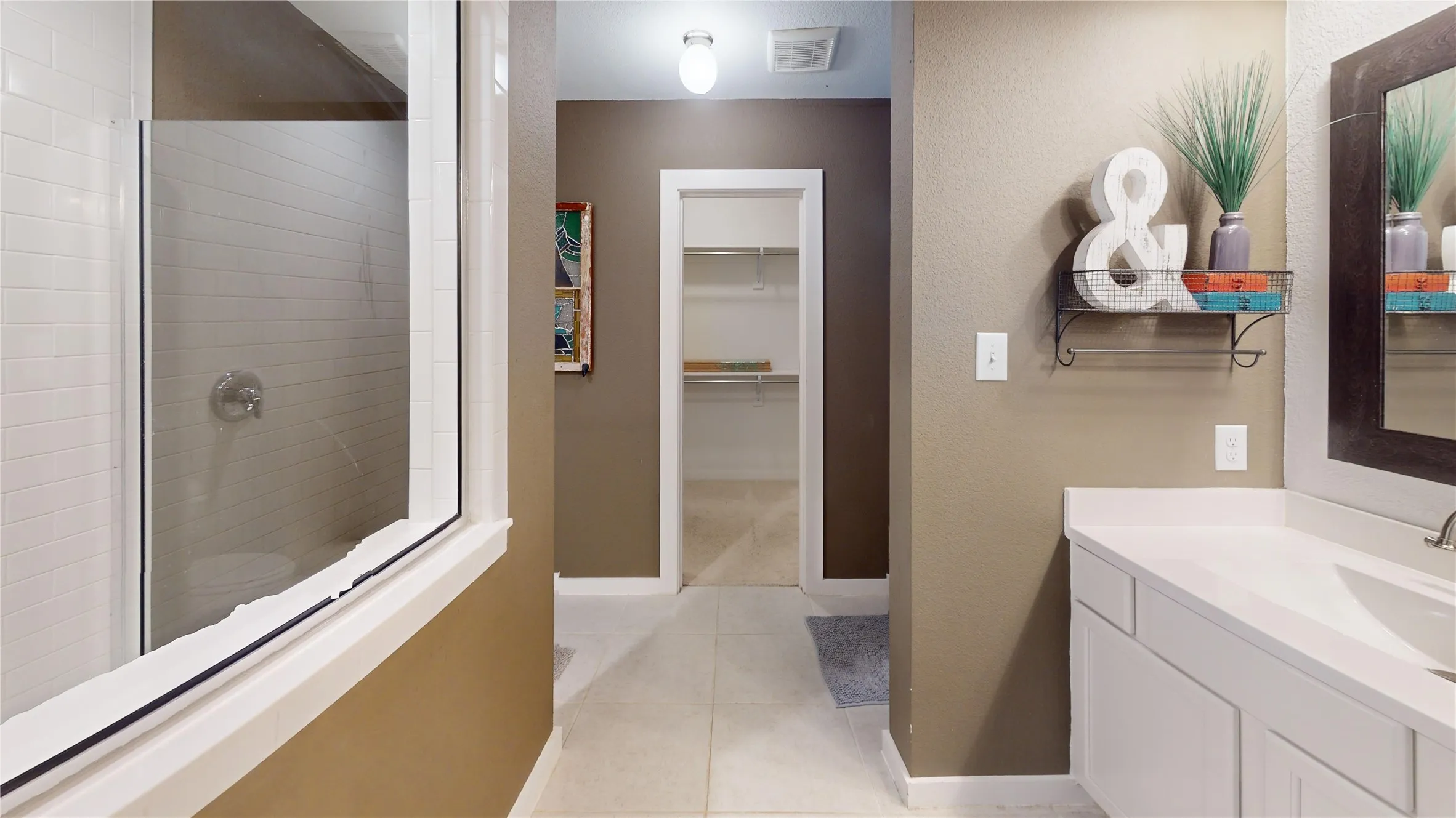 Bathroom featuring a walk-in shower with subway tile, white vanity with integrated sink, rectangular framed mirror, and tile flooring