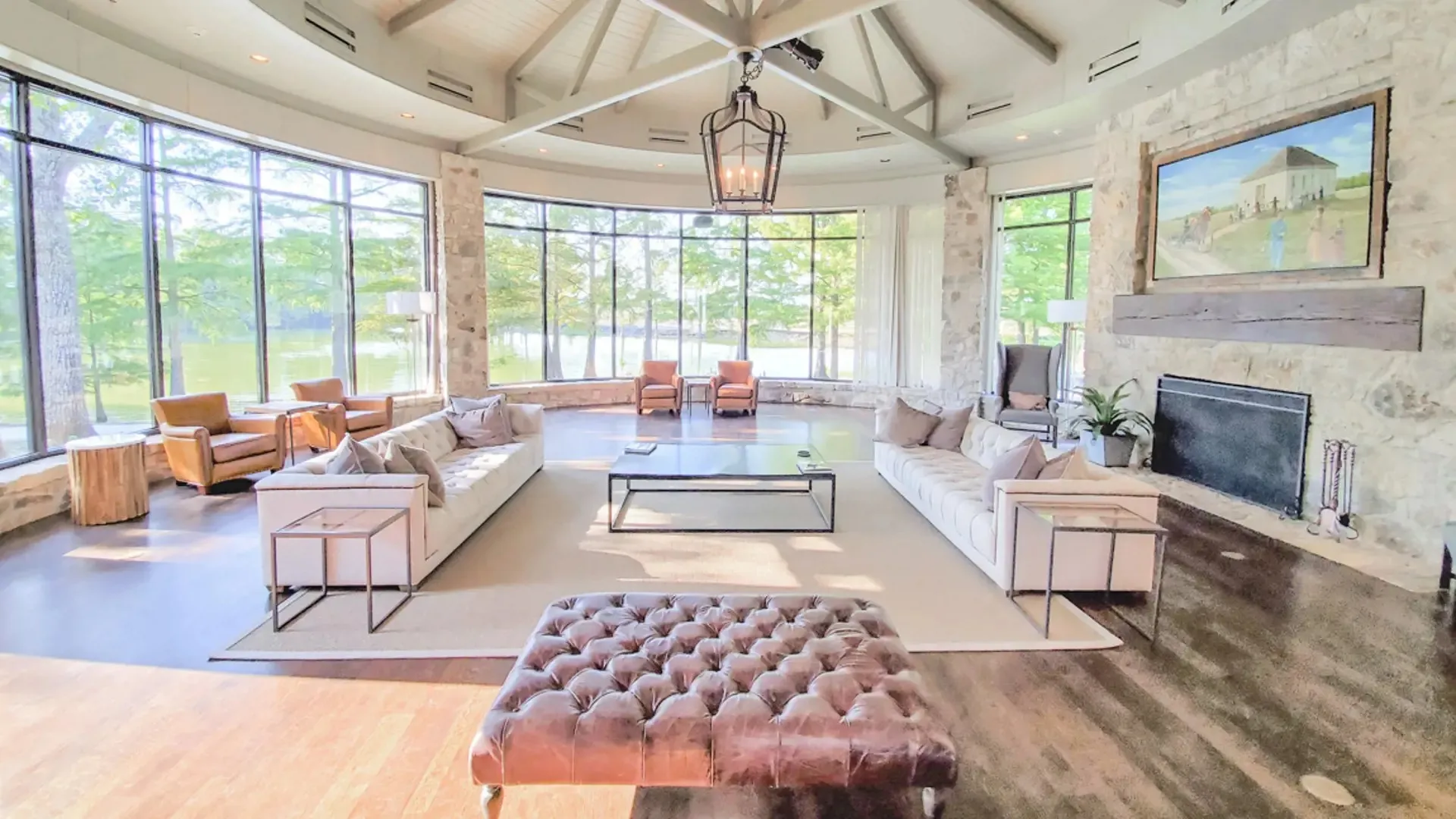 Spacious living area featuring expansive floor-to-ceiling windows, a stone fireplace with a substantial wood mantel, a vaulted ceiling with exposed beams, and integrated ceiling vents