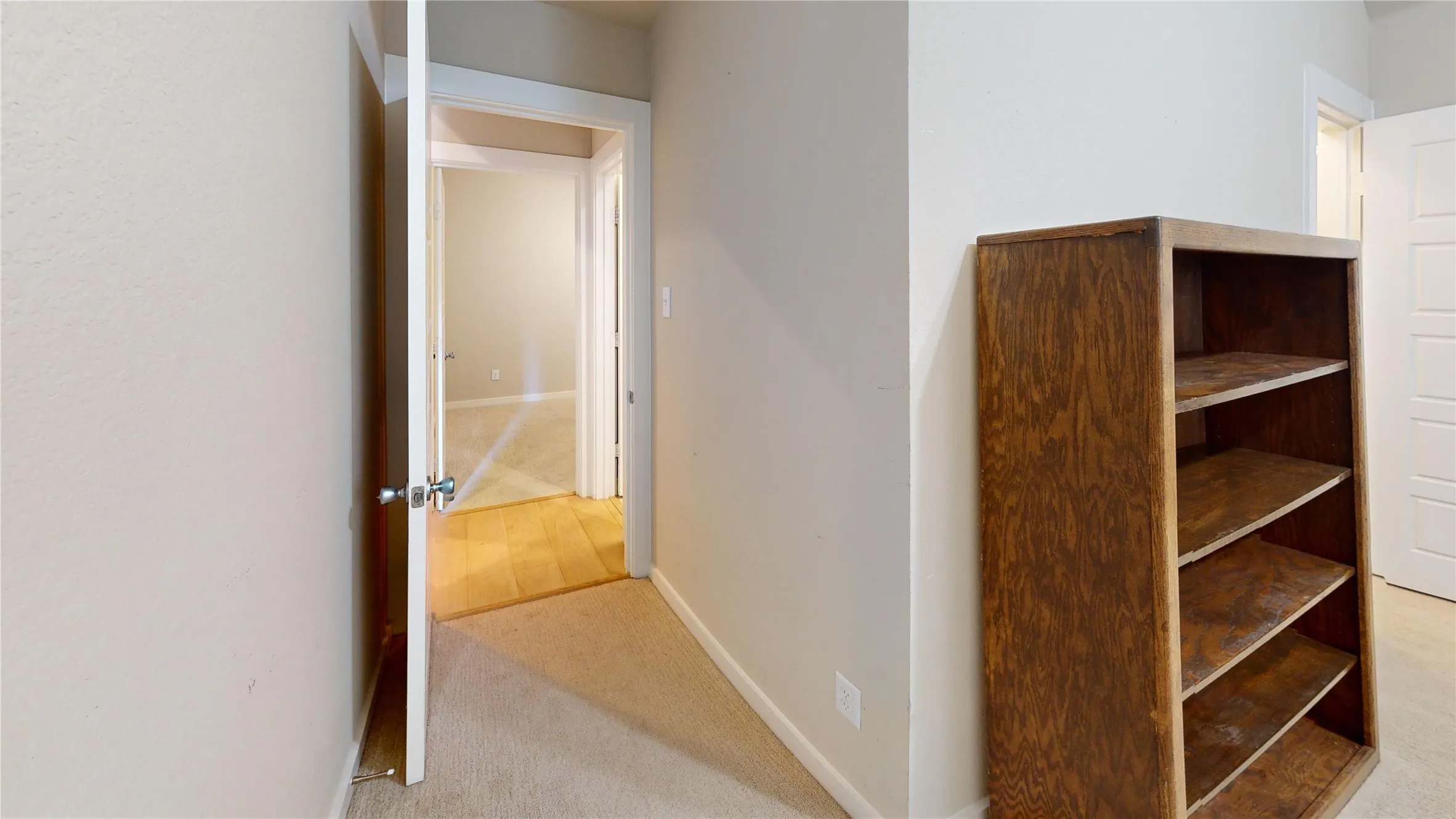 Hallway featuring light-toned walls, neutral carpet, and a wood-finish open shelving unit