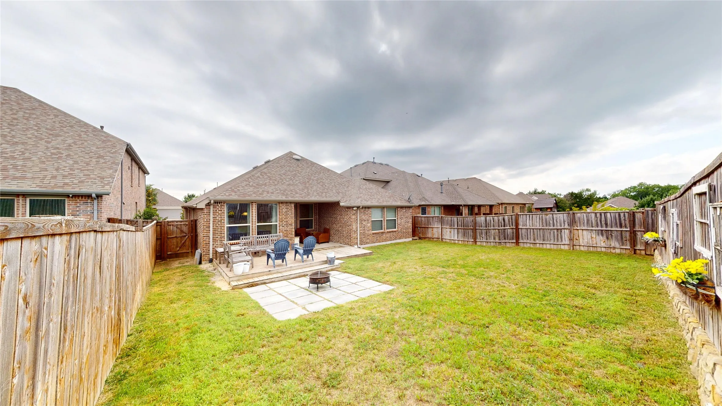 Expansive backyard featuring a manicured lawn, full wood fencing, a dedicated patio area, and a fire pit