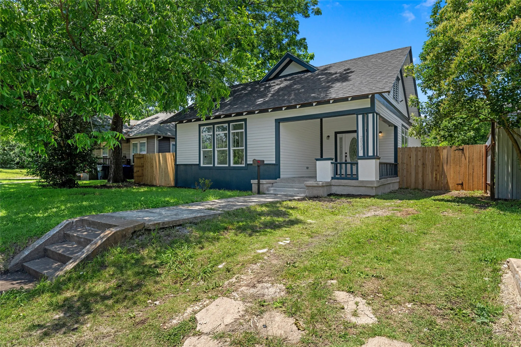 Charming bungalow featuring a covered front porch, white siding with dark trim, a gabled roof, and a mature front yard tree