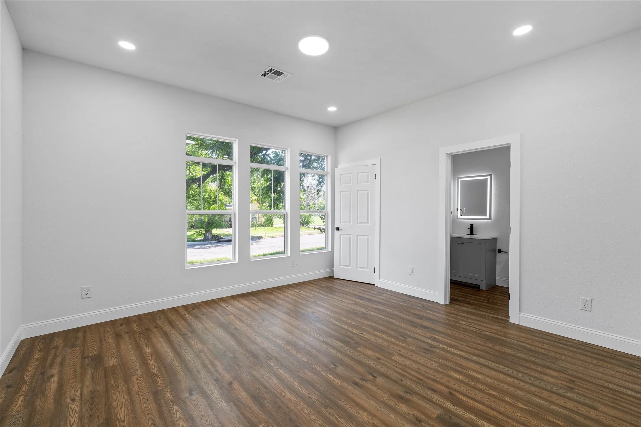 Spacious room featuring wood-finish flooring, recessed lighting, and three tall windows