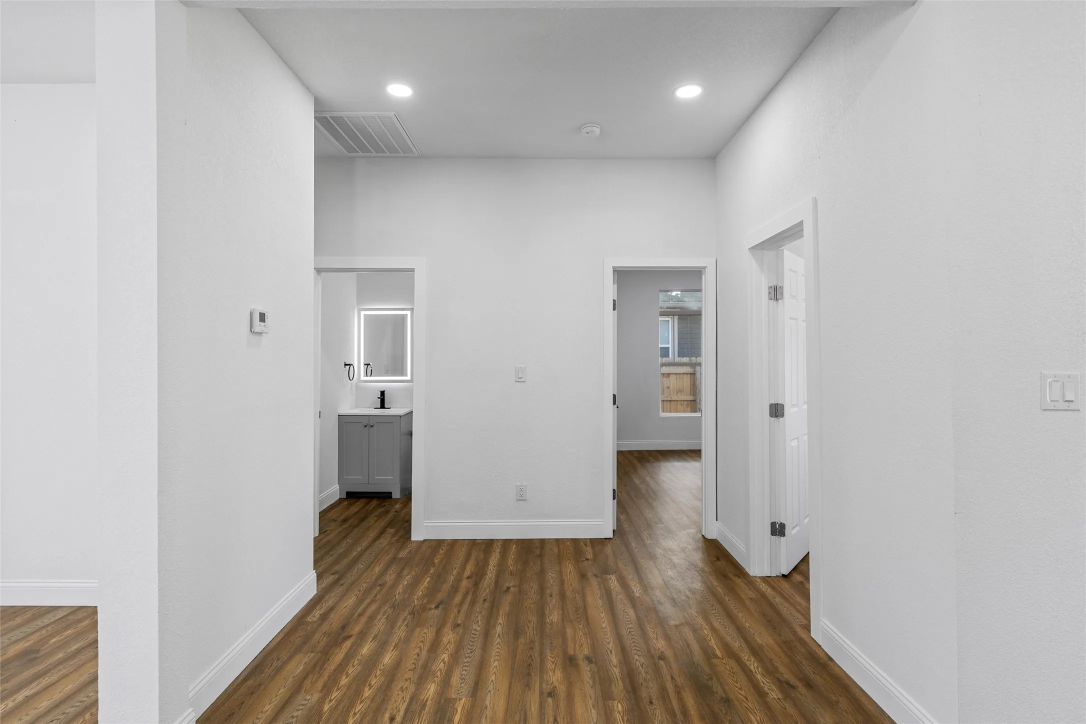 Hallway featuring wood-finish flooring, white baseboards, and bright white walls