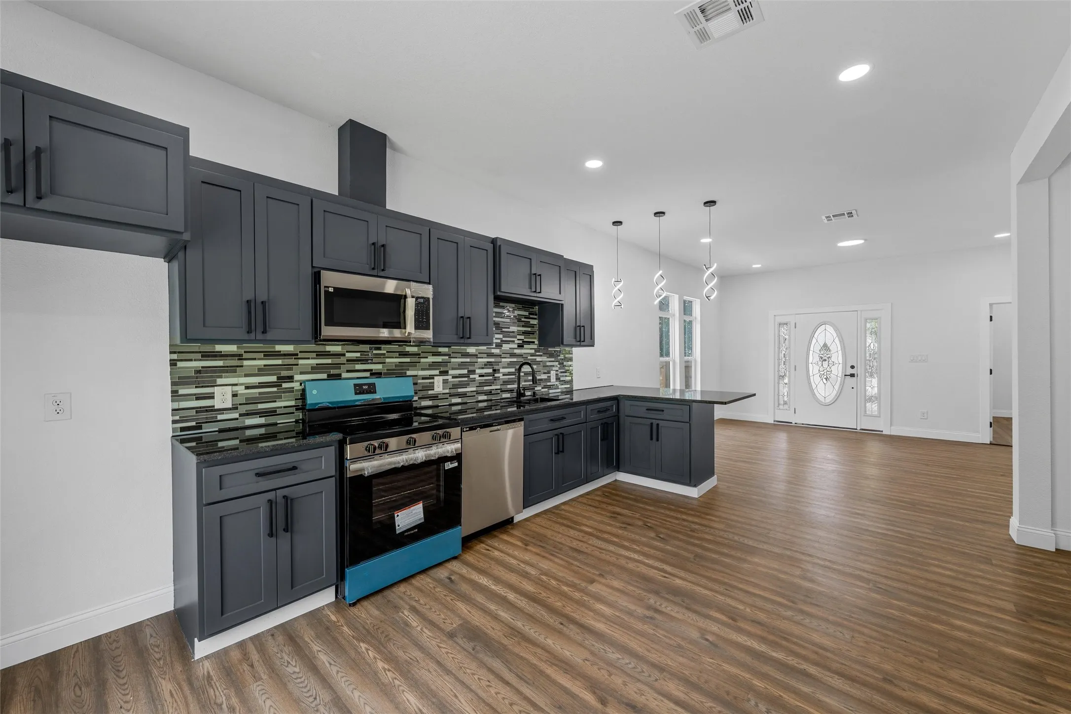 Modern kitchen featuring dark cabinetry, stainless steel appliances, a mosaic tile backsplash, and sleek pendant lighting
