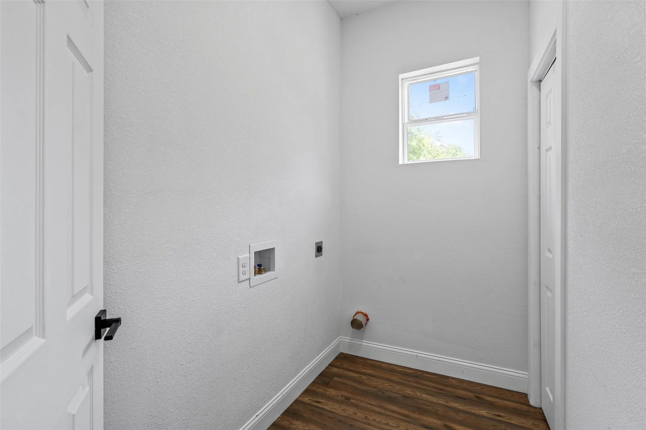 Dedicated utility space featuring a window, wood-finish flooring, white baseboards, and a white paneled door with black hardware