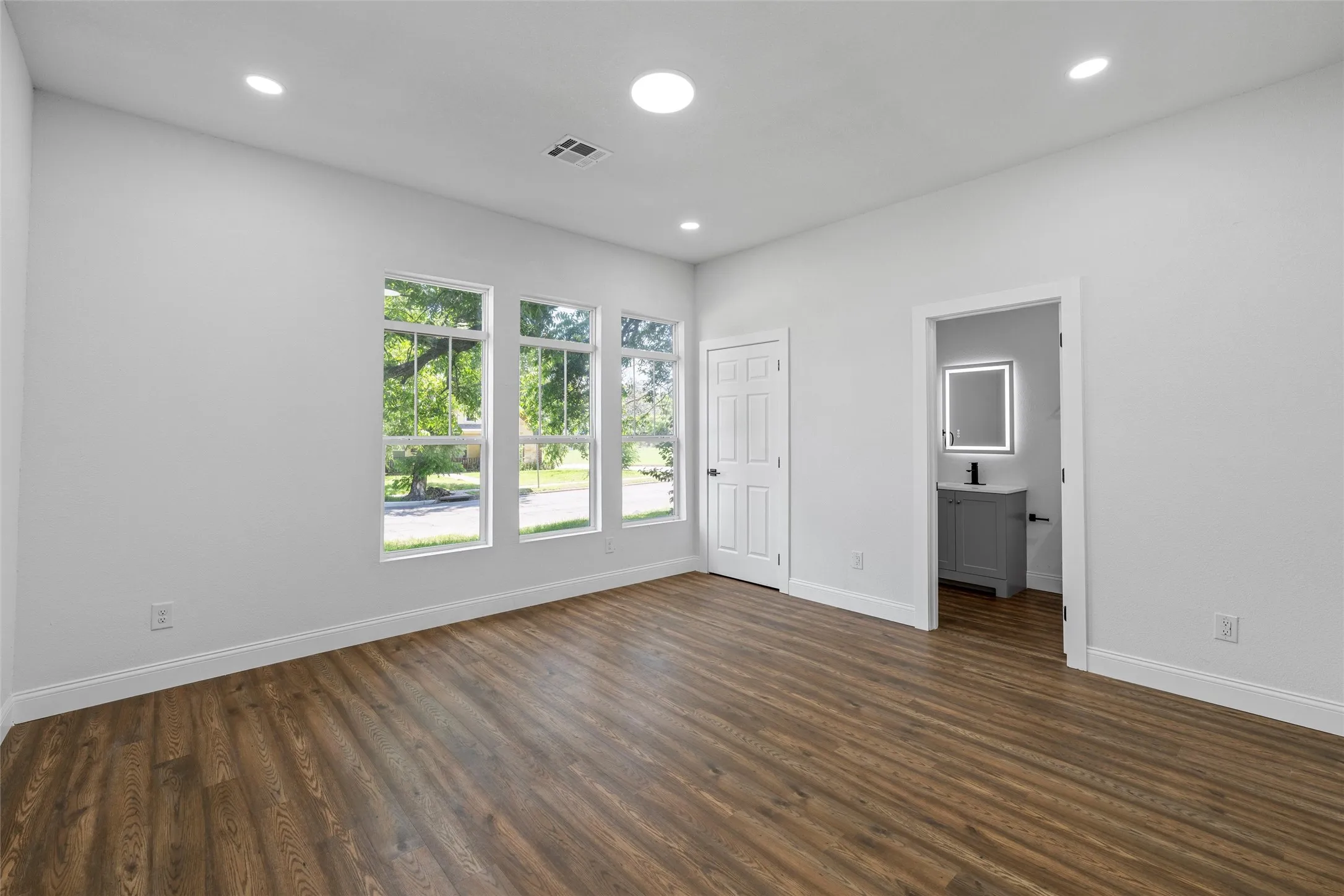 Spacious room featuring three large windows, recessed lighting, and wood-finish flooring