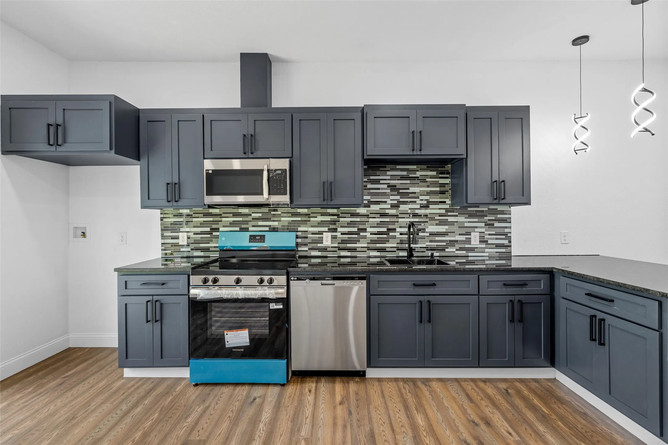 Modern kitchen featuring dark cabinetry with black hardware, stainless steel appliances, and a mosaic tile backsplash