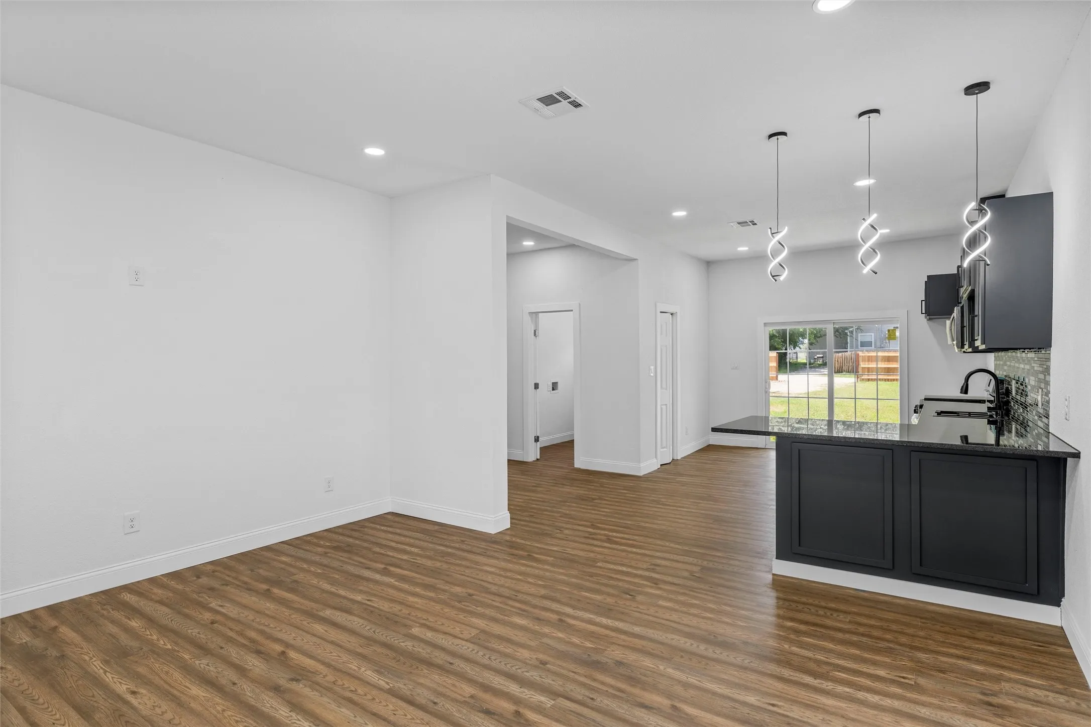 Open-concept living space featuring wood-finish flooring, recessed lighting, and a kitchen island with dark cabinetry and a dark countertop