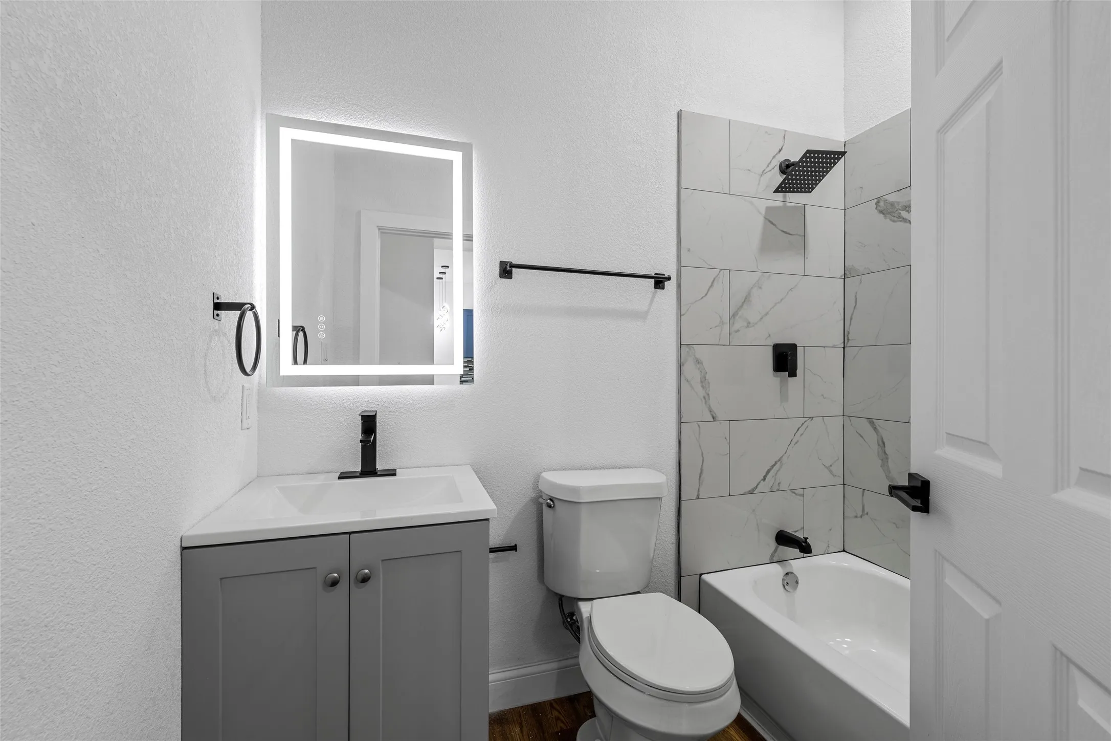 Bathroom featuring a gray vanity with an integrated sink, an illuminated mirror, and a tiled shower with matte black fixtures