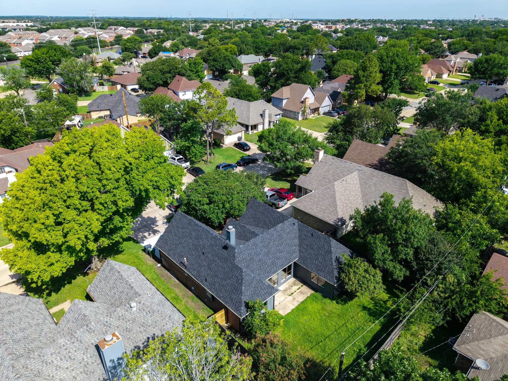 Aerial perspective showcasing a residential property with a dark shingle roof and a spacious backyard featuring green lawn space