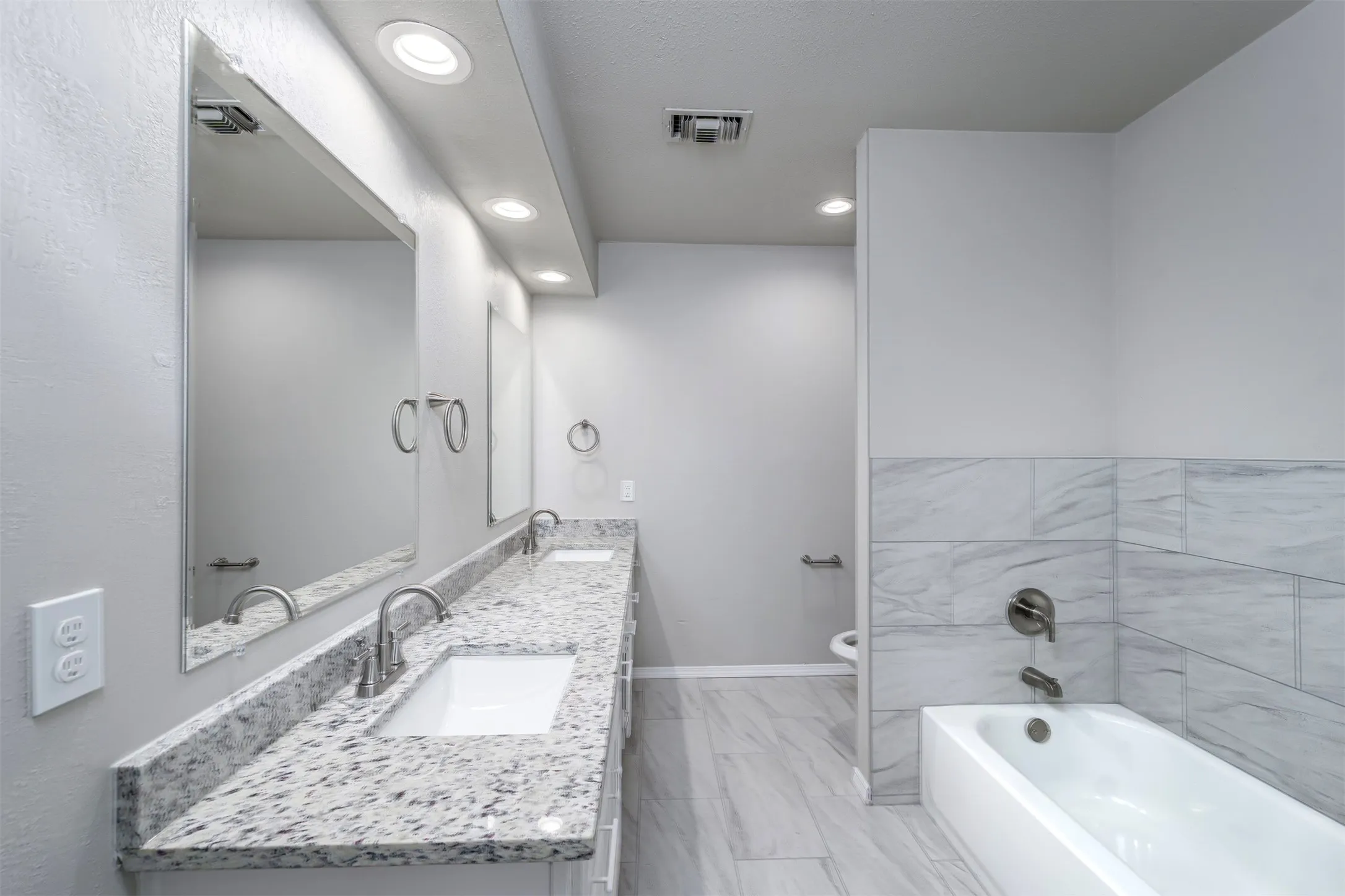 Bathroom featuring a dual vanity with granite-finish countertops, undermount sinks, and brushed nickel fixtures