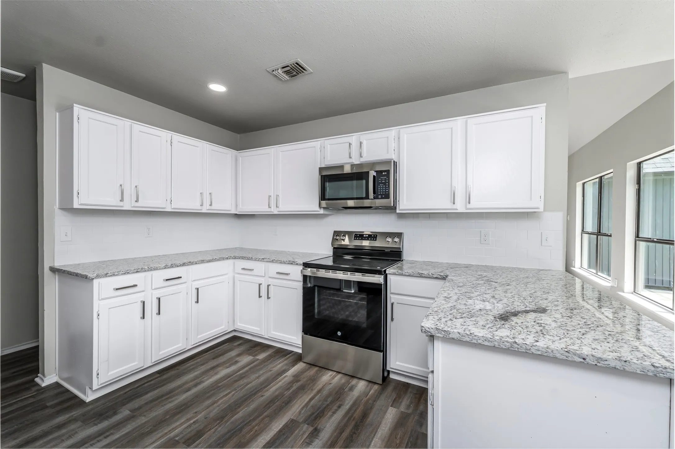 Kitchen featuring white cabinetry, light-toned countertops, stainless steel appliances, and wood-finish flooring
