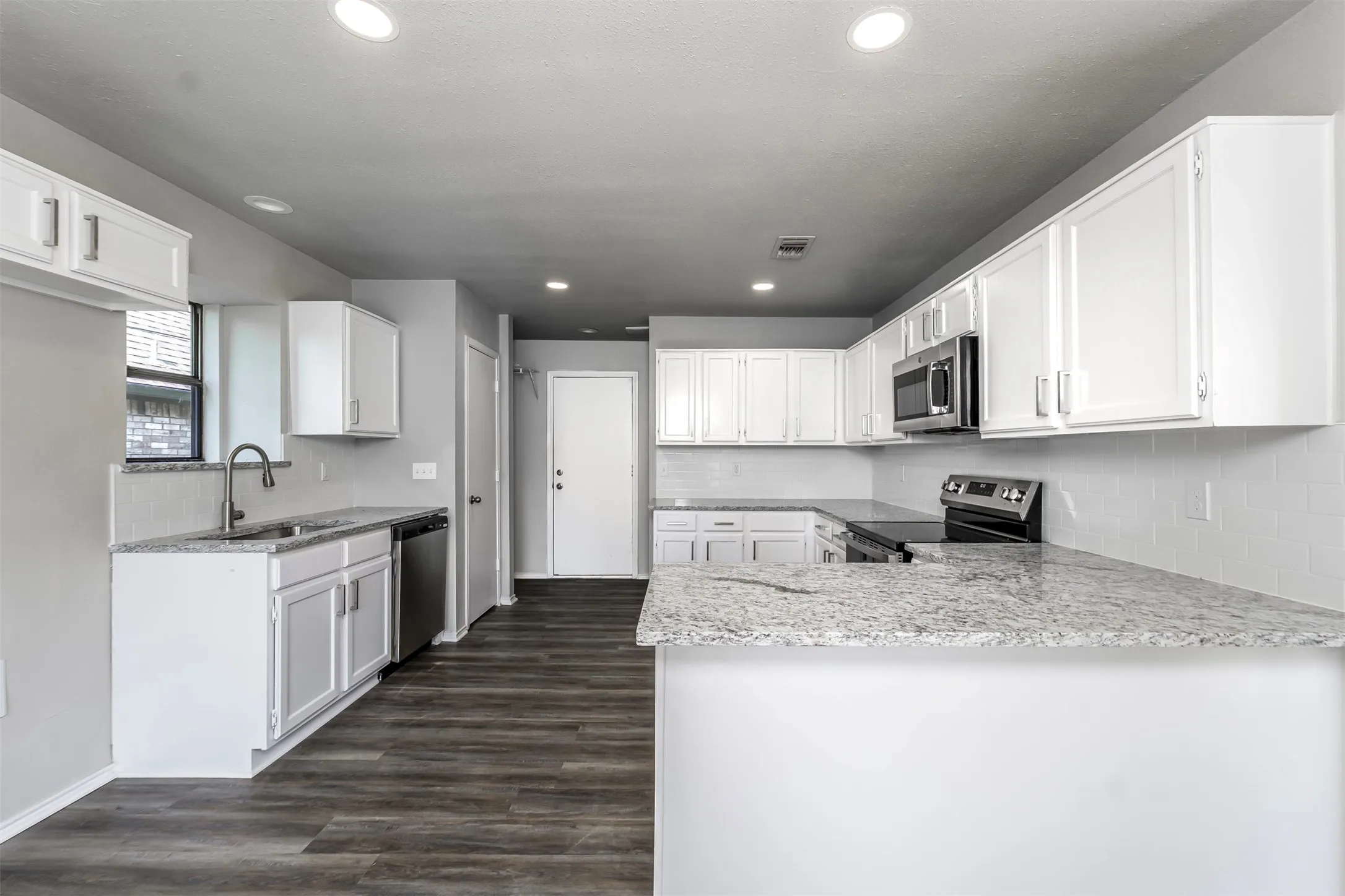 Galley kitchen featuring white cabinetry, stainless steel appliances, speckled stone countertops, a white tile backsplash, and wood-finish flooring