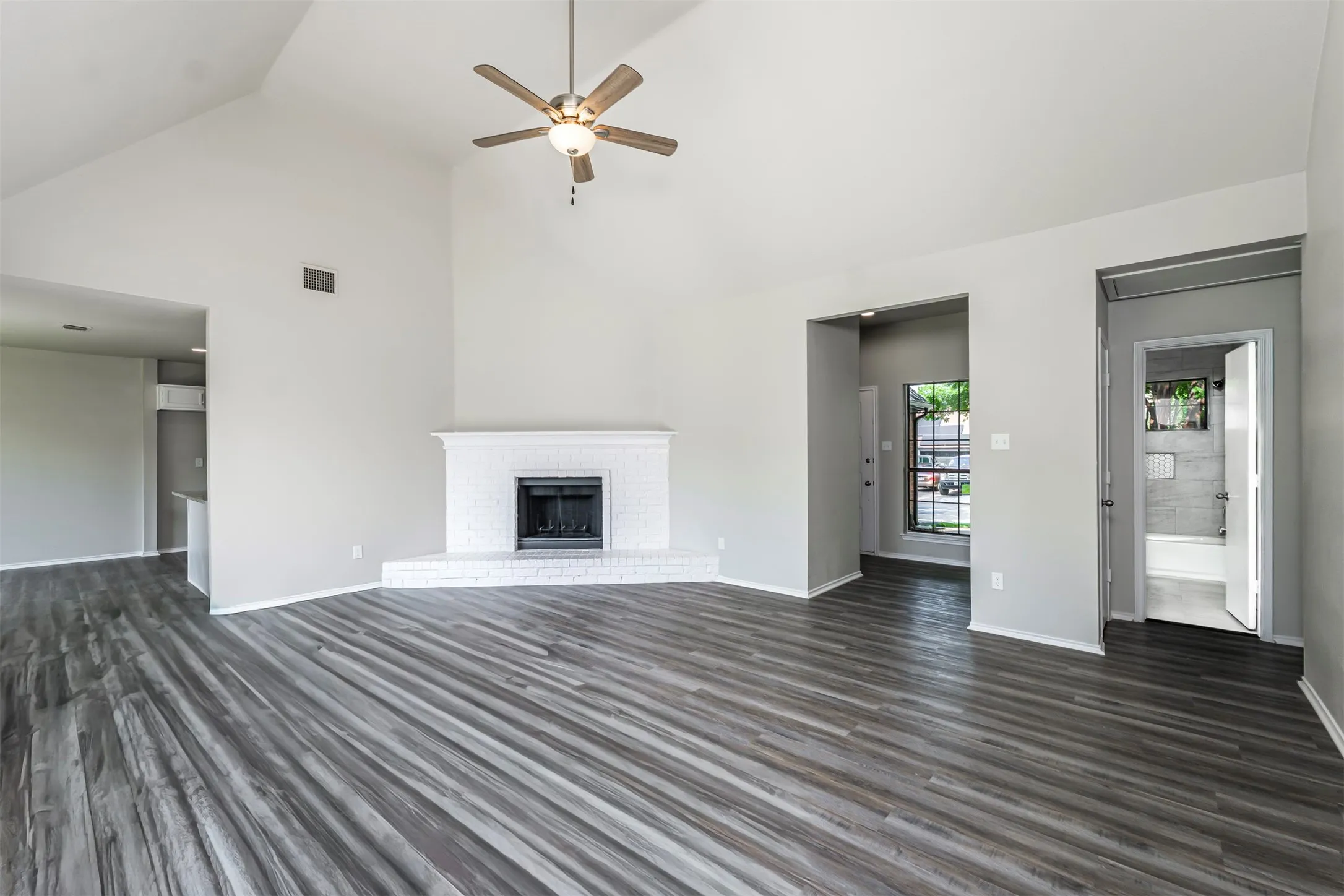 Spacious living area featuring vaulted ceilings, a ceiling fan, and wood-finish flooring