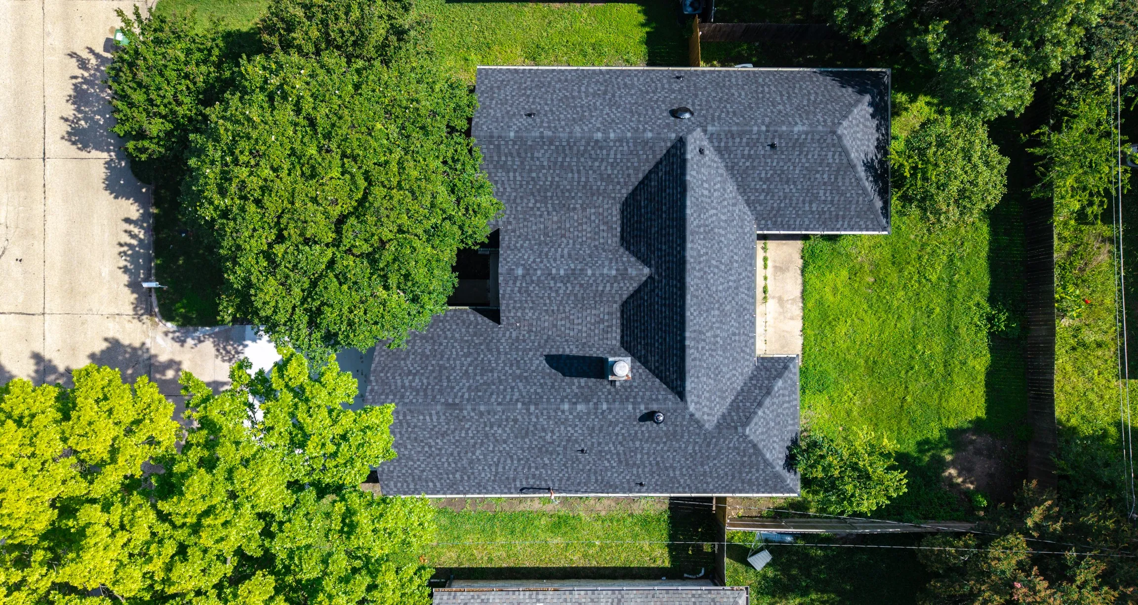 Dark shingle roof, well-maintained lawn, mature trees, concrete drive, and adjacent paved area