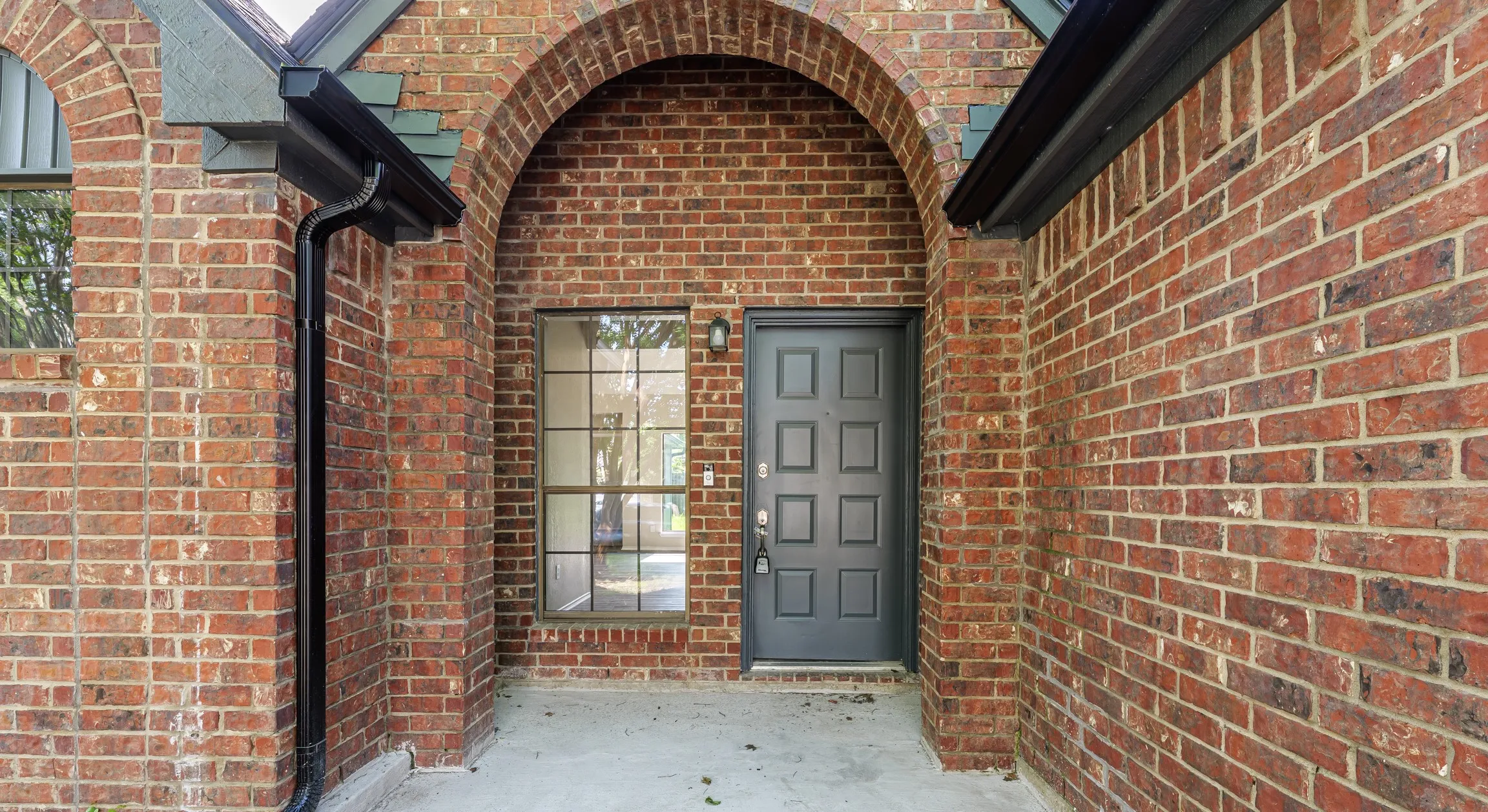 Brick facade entry featuring a paneled door, arched doorway, and grid-pattern window