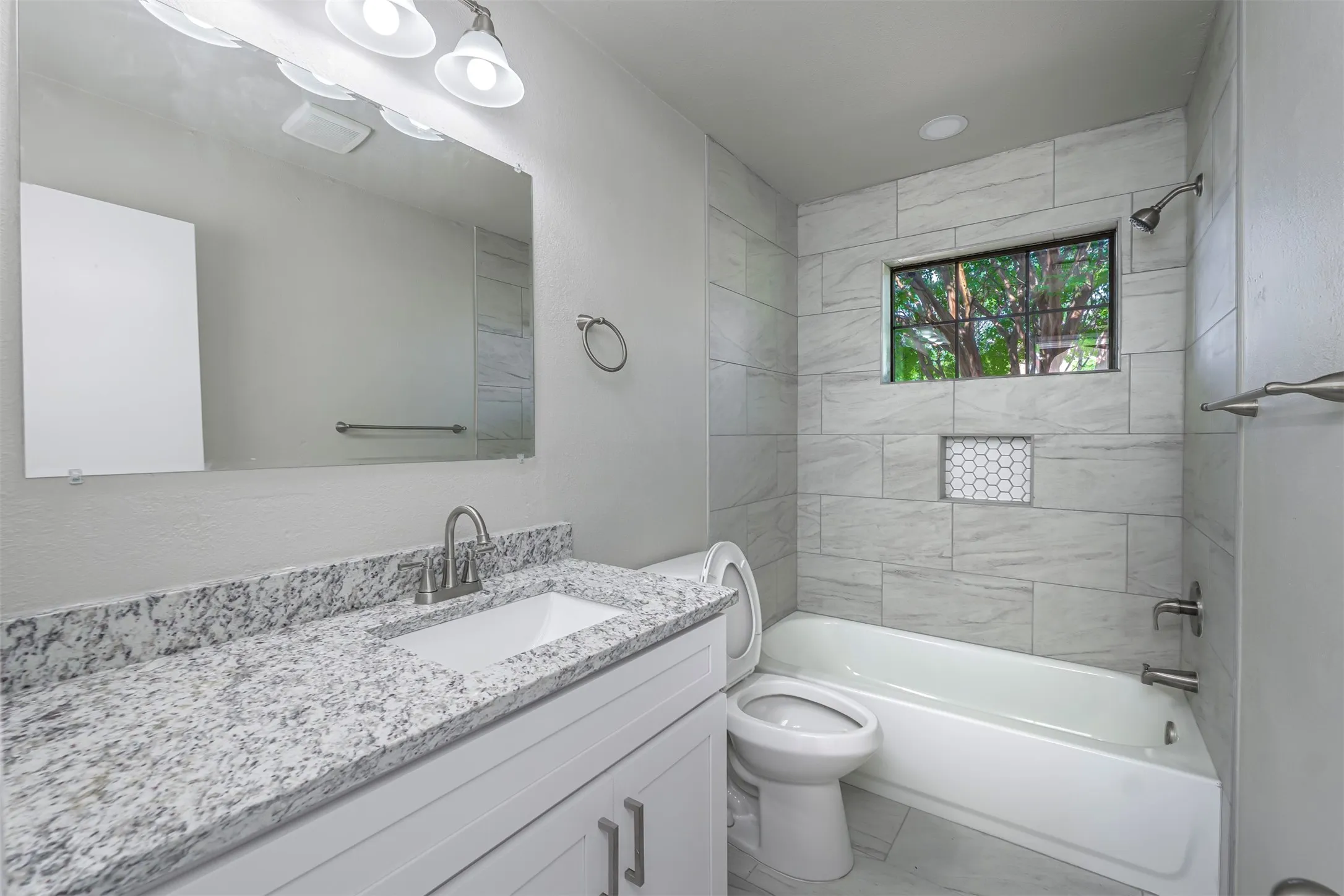Bathroom featuring a white vanity with a speckled countertop, a large mirror, and a white bathtub