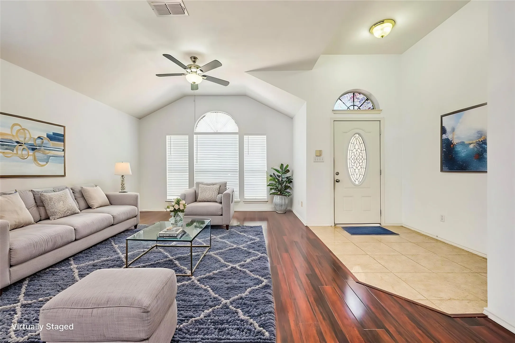 Vaulted ceiling with ceiling fan, wood-finish flooring, arched transom window, entry door with decorative glass, and tile flooring in the entry