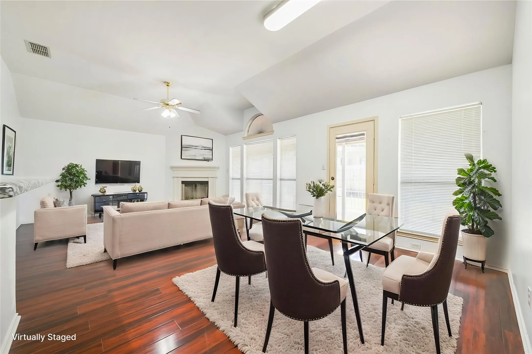 Vaulted ceilings, wood-finish flooring, fireplace, large windows, and a ceiling fan
