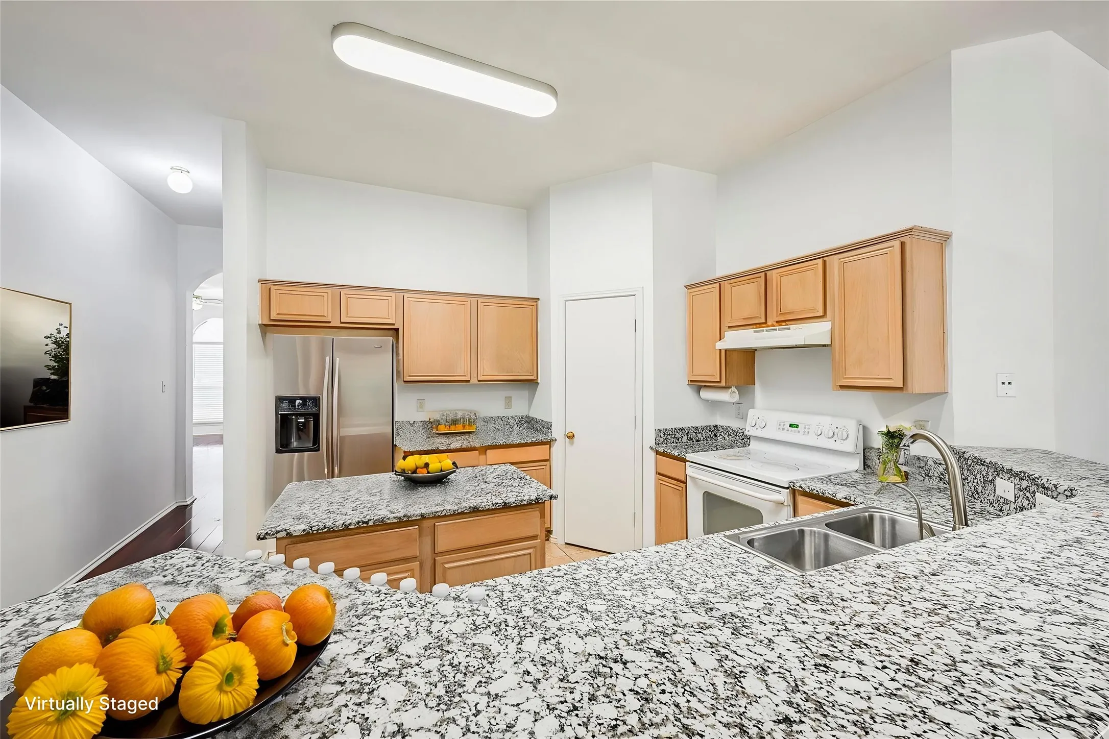 Kitchen featuring a stainless steel French door refrigerator, light wood cabinetry, stone-finish countertops, and a double basin stainless steel sink with a gooseneck faucet