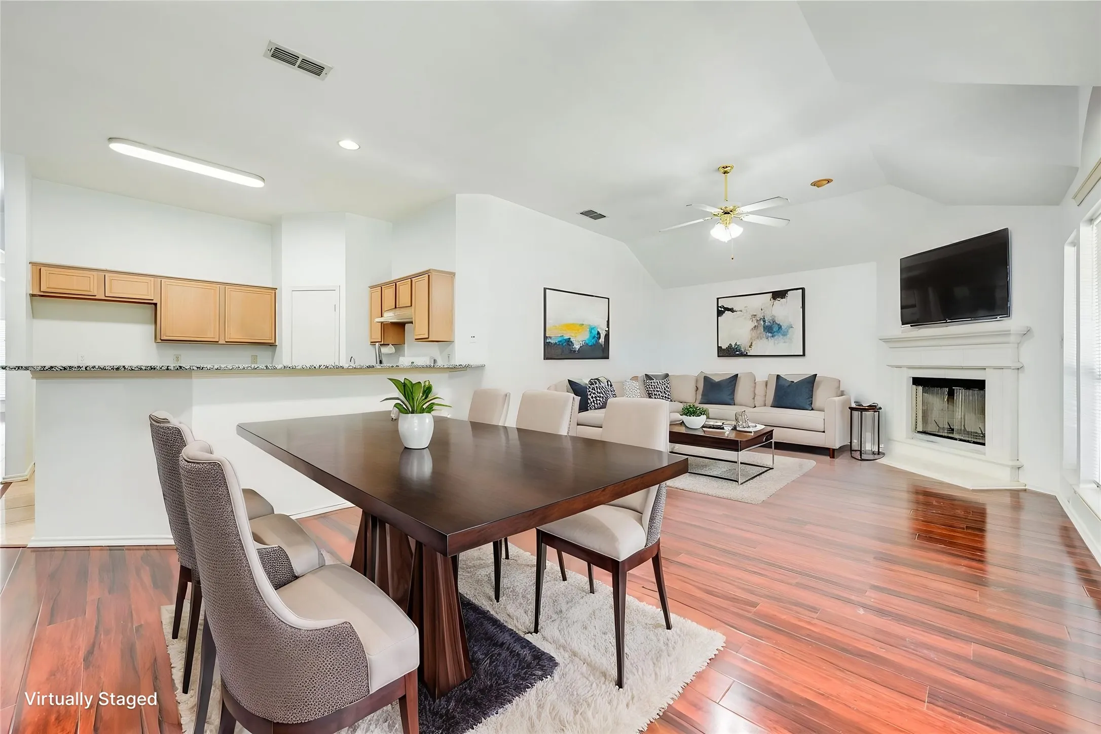 Vaulted ceilings, wood-finish flooring, and a corner fireplace with a white mantel