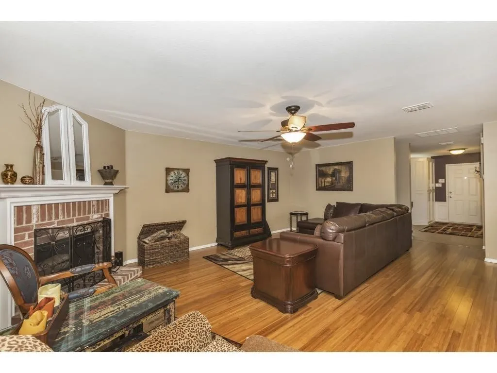 Living area featuring wood-finish flooring, a brick-front fireplace with a white mantel, and a ceiling fan with integrated lighting