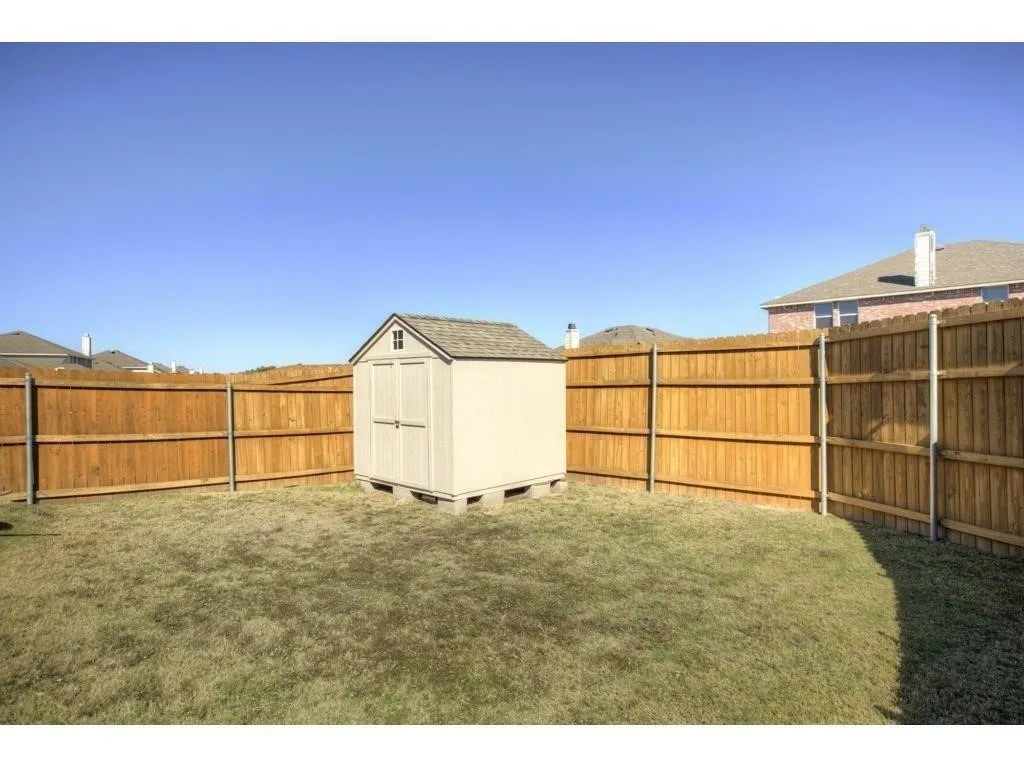 Fenced backyard featuring a storage shed with a shingle roof