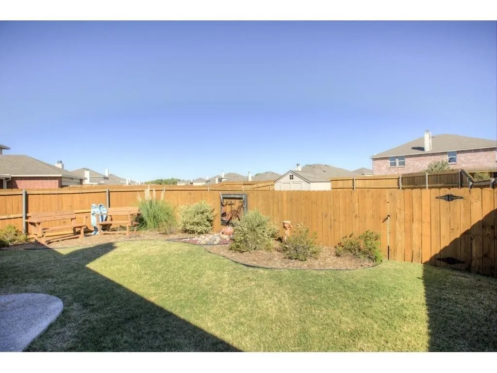 Spacious backyard featuring a wooden privacy fence, a manicured lawn, and a landscaped garden bed