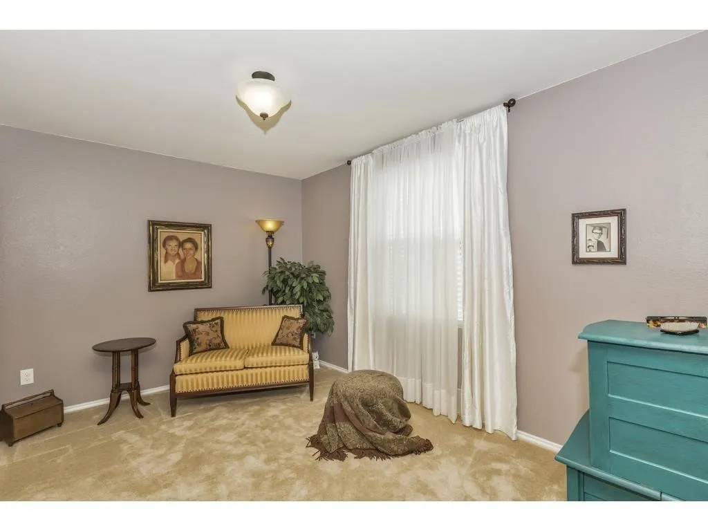 Spacious room featuring neutral paint tones, light-colored carpeting, a large window with white drapes, and a semi-flush mount ceiling light fixture