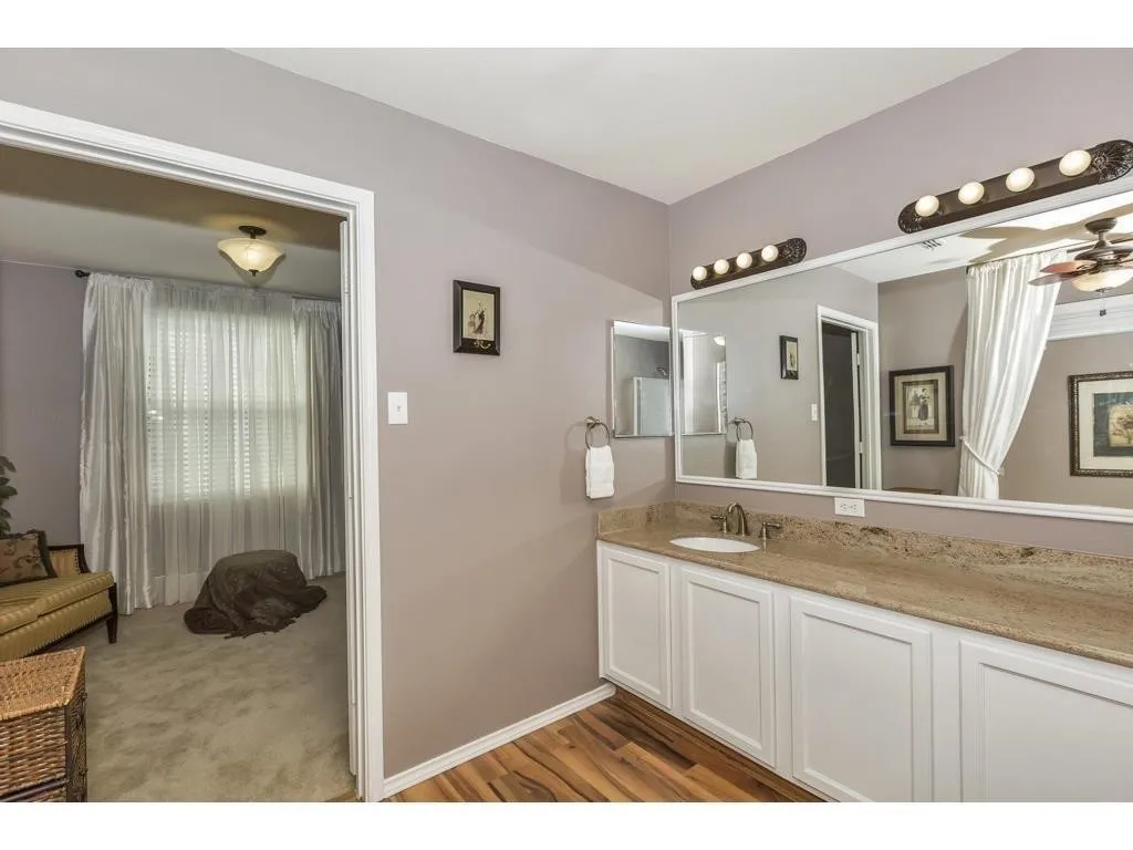 Vanity area featuring a stone countertop, white cabinetry, integrated sink, and wood-finish flooring