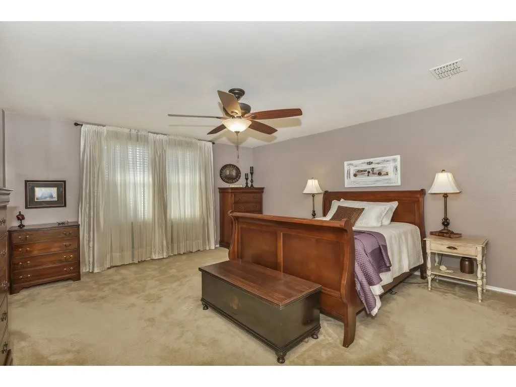 Spacious room featuring neutral carpeting, a ceiling fan with integrated lighting, and expansive windows dressed with privacy blinds and sheer curtains